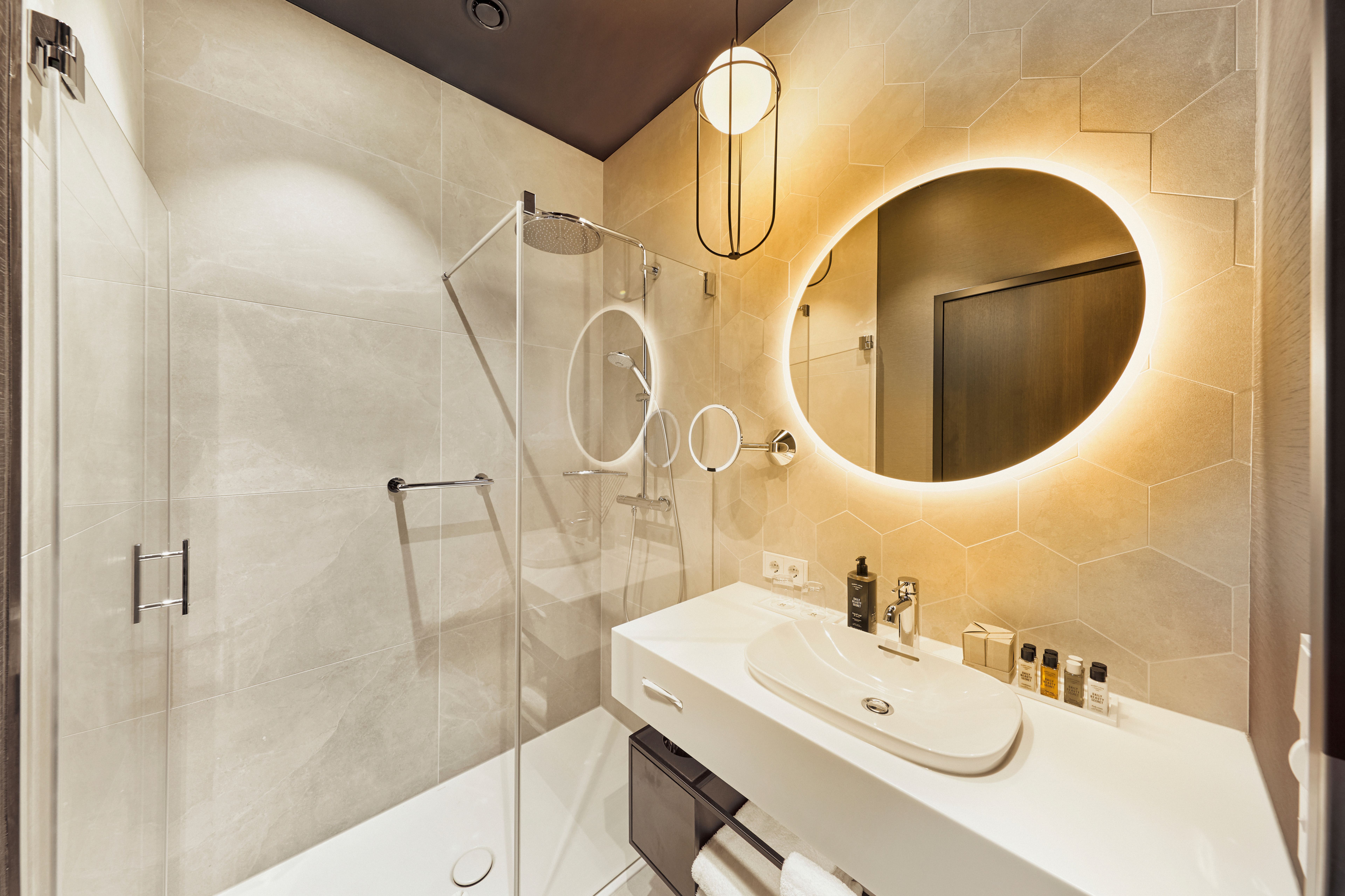 Modernes Badezimmer mit beleuchtetem ovalem Spiegel, weißem Waschbecken, Dusche mit Glasabtrennung und stilvoller Beleuchtung, die eine entspannte und elegante Atmosphäre schafft. Modernes Badezimmer mit beleuchtetem ovalem Spiegel, weißem Waschbecken, Dusche mit Glasabtrennung und stilvoller Beleuchtung, die eine entspannte und elegante Atmosphäre schafft.