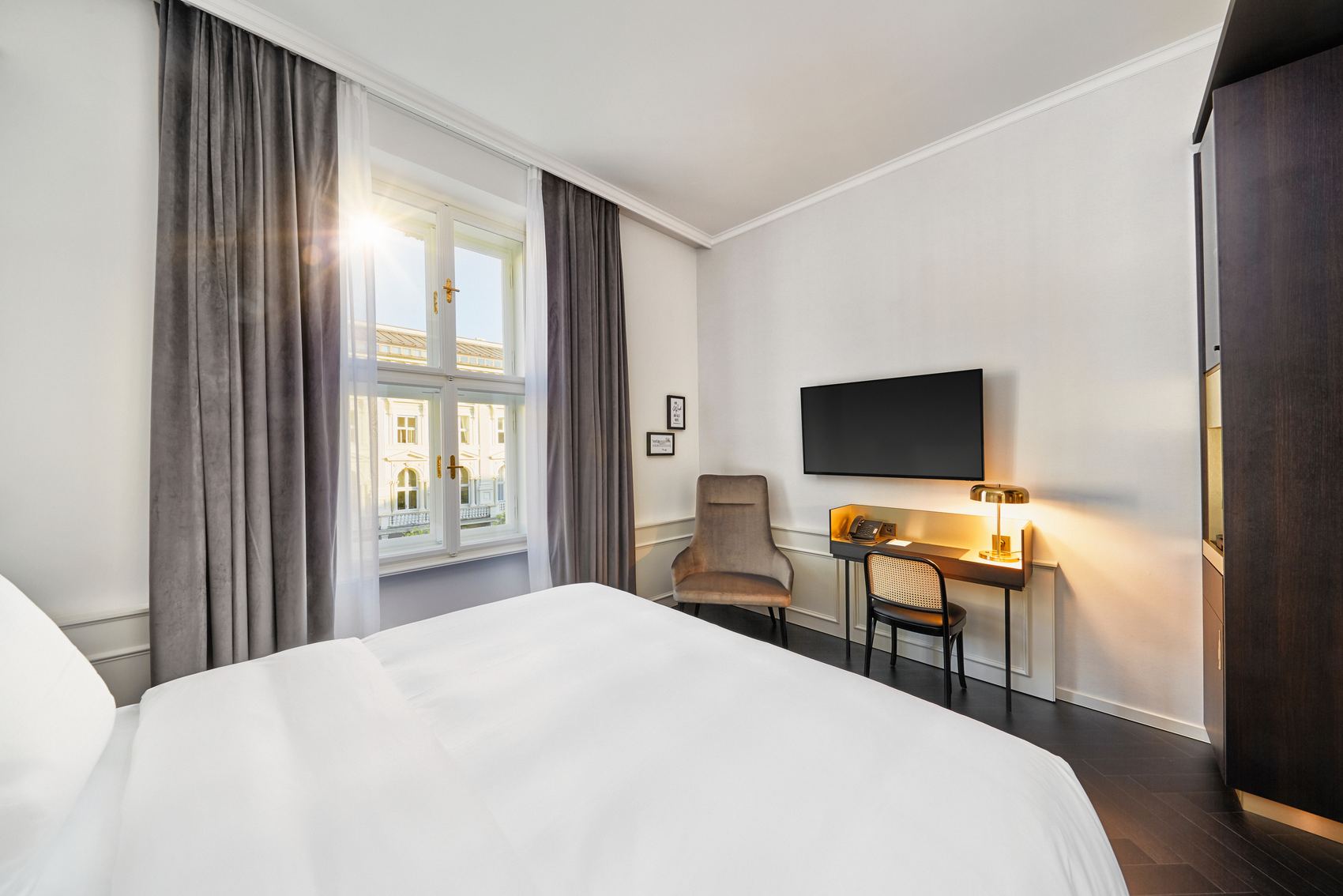 Helles, modern eingerichtetes Hotelzimmer mit großem Fenster, gemütlichem Bett, Schreibtisch, Fernseher und bequemen Stuhl. Ruhige, freundliche Atmosphäre für Erholung und Arbeit.