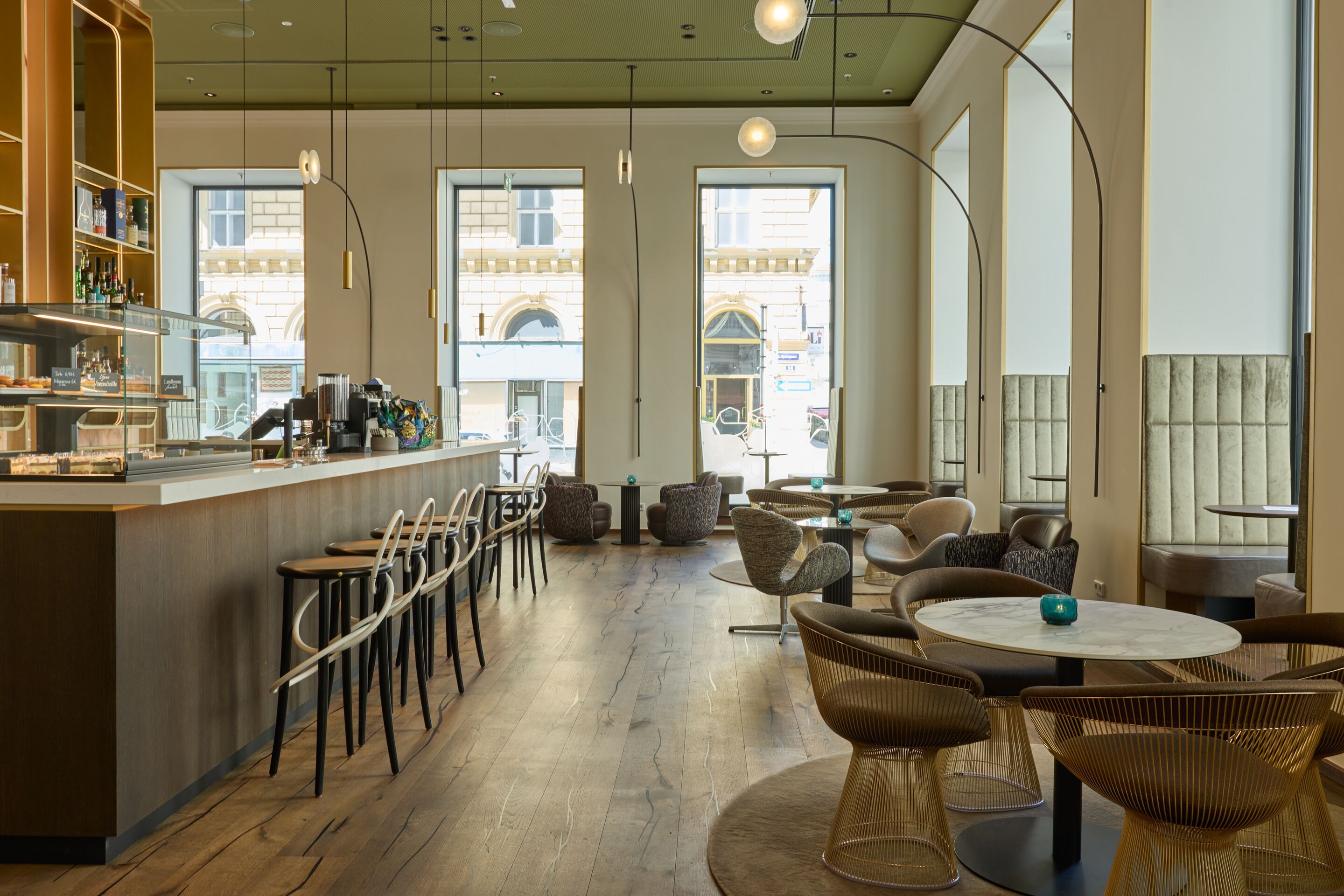 Helles, modernes Café mit hohen Fenstern, gemütlichen Sitzbereichen und Barhockern. Warme Holzböden, dezente Beleuchtung und stilvolles Mobiliar schaffen eine einladende Atmosphäre zum Entspannen und Genießen.