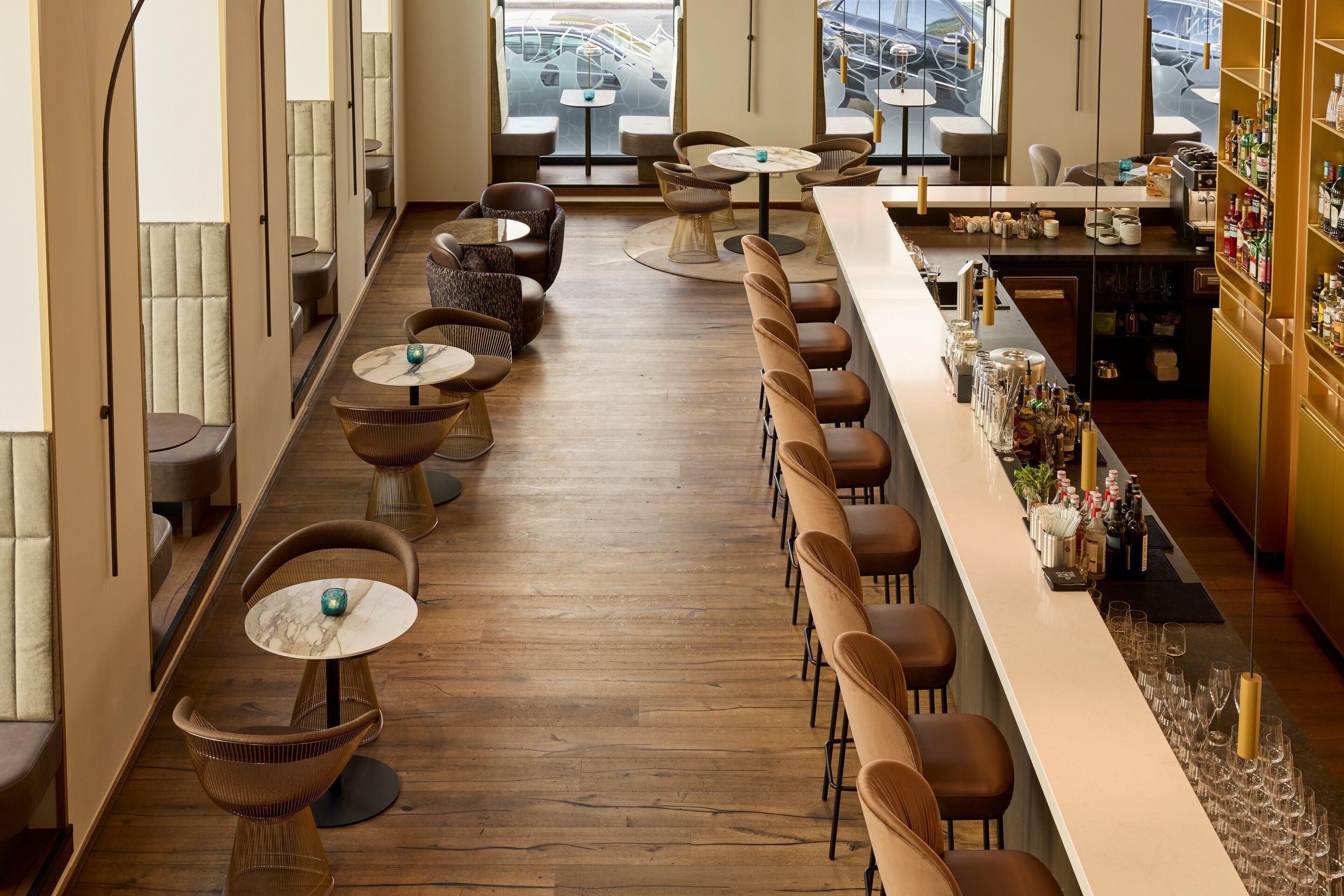 Moderne Hotelbar mit Lederhockern, gemütlichen Sitzgruppen und Holzboden. Große Fenster bieten Blick auf einen Hafen mit Booten. Stilvolle Atmosphäre für Entspannung und geselliges Beisammensein.