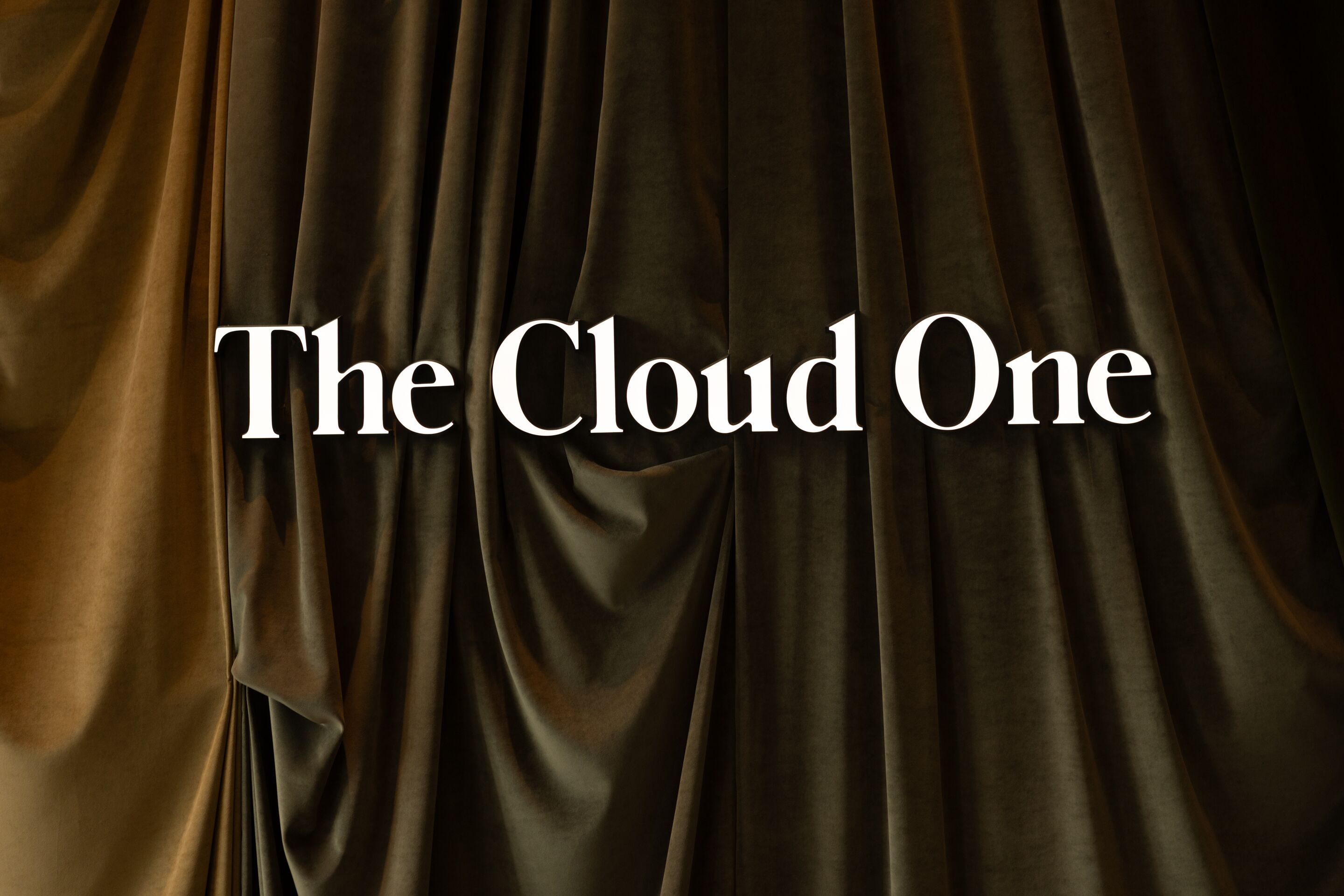 Schriftzug „The Cloud One“ vor dunkelgrünem, samtigem Vorhang, der eine elegante und luxuriöse Atmosphäre vermittelt.