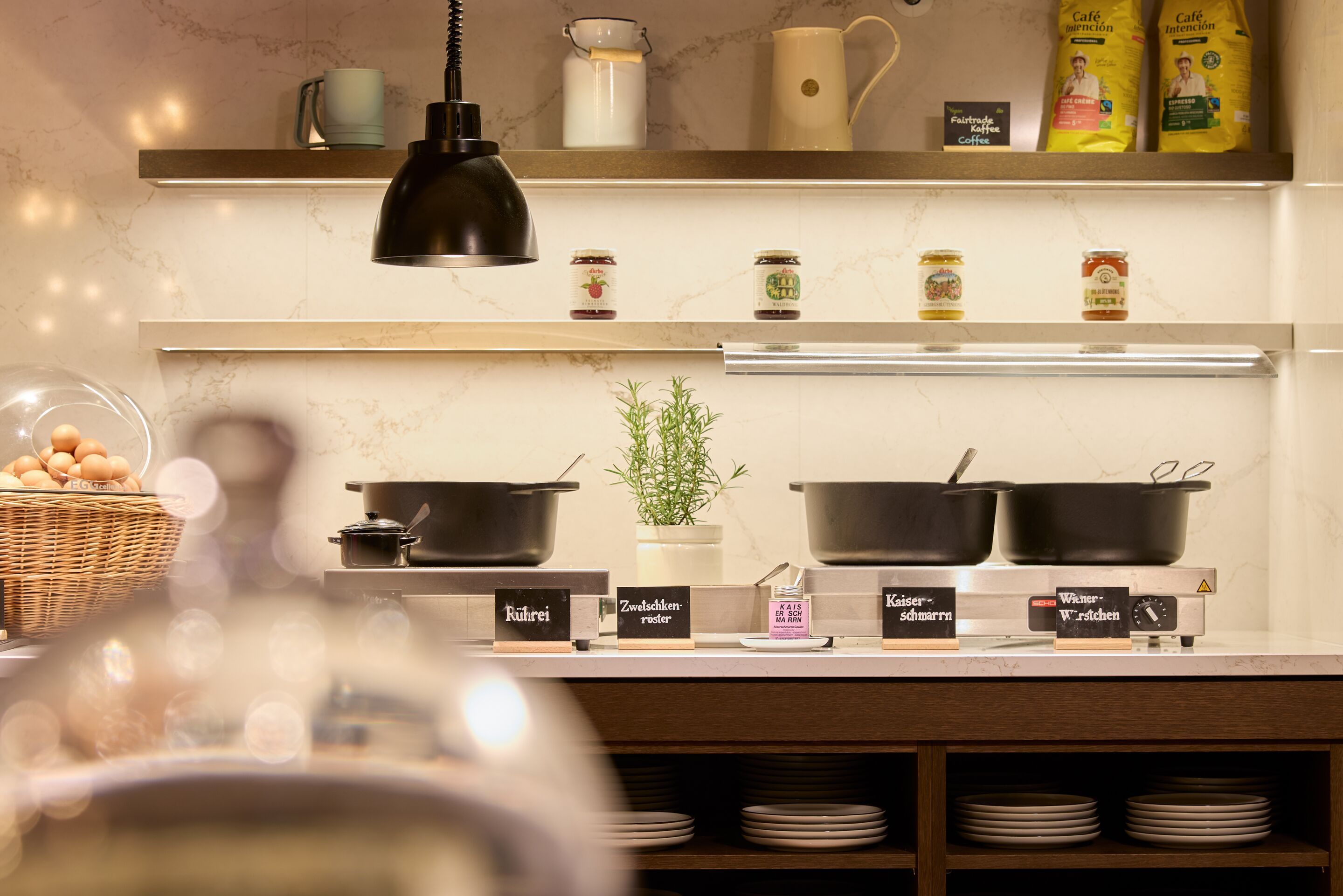 Gemütliche Buffetstation mit warmen Speisen in schwarzen Töpfen, frischen Kräutern und Eierkorb, ideal für ein herzhaftes Frühstück oder gemütliches Abendessen in entspannter Atmosphäre.