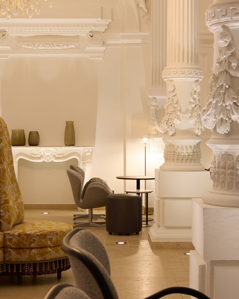 Eleganter Hotel-Loungebereich mit kunstvollen Stuckverzierungen, gemütlichen Sesseln und warmem Licht, das eine einladende Atmosphäre für entspannte Momente schafft.