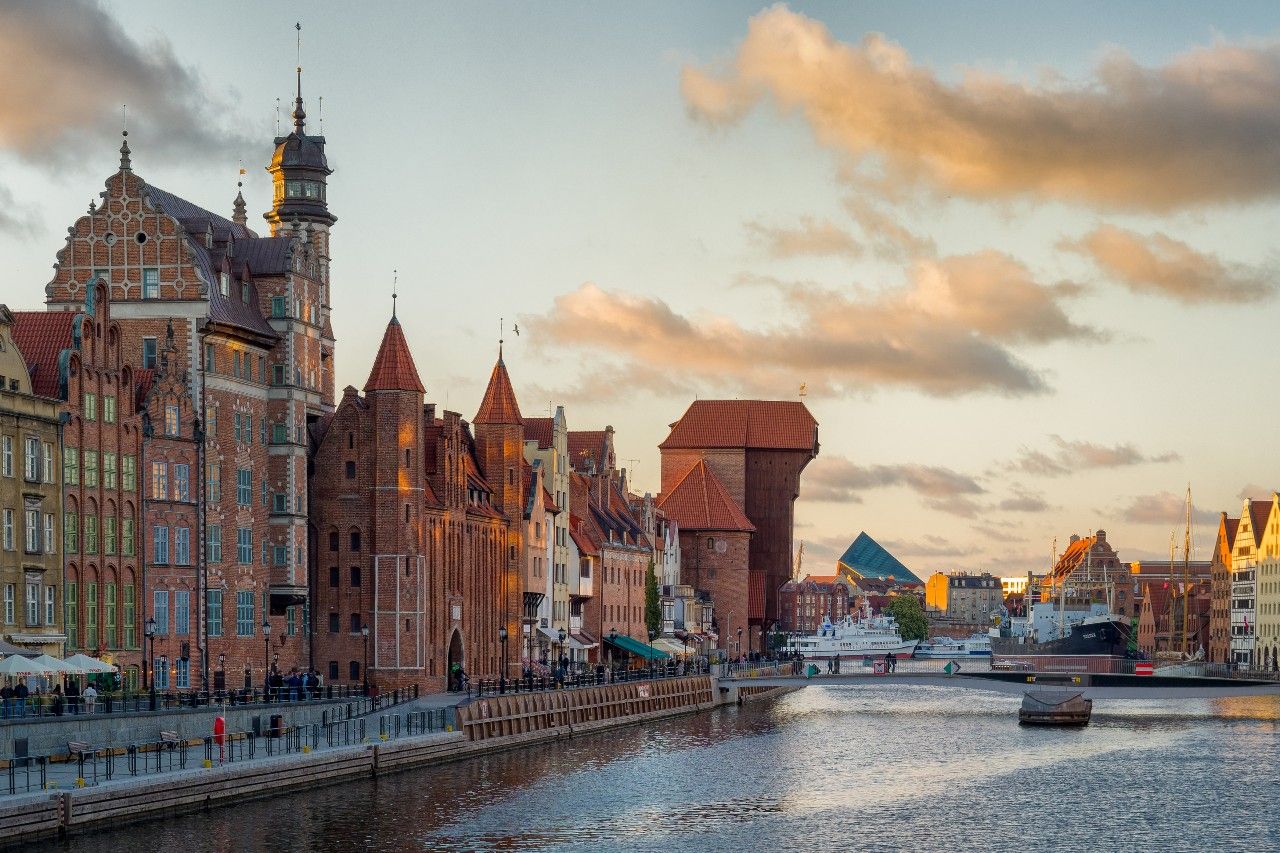 Historische Giebelhäuser und der berühmte Krantor am Ufer der Motława in Danzig bei Sonnenuntergang, mit ruhigem Wasser und schönem Himmel.