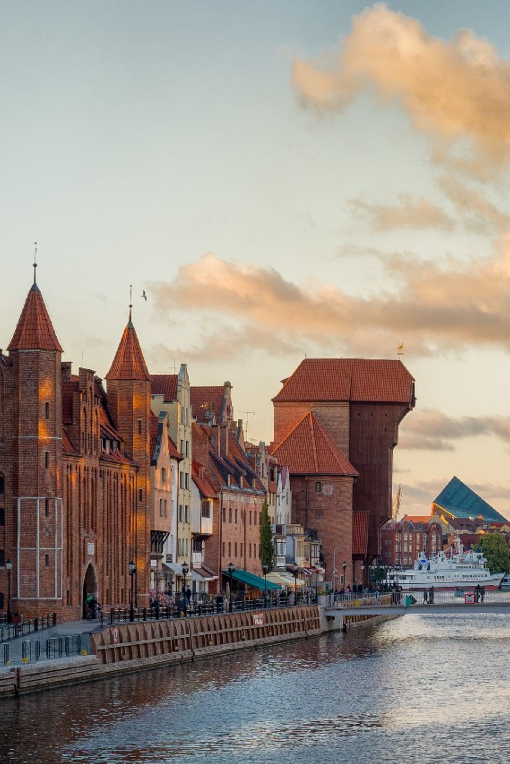 Historische Giebelhäuser und der berühmte Krantor am Ufer der Motława in Danzig bei Sonnenuntergang, mit ruhigem Wasser und schönem Himmel.