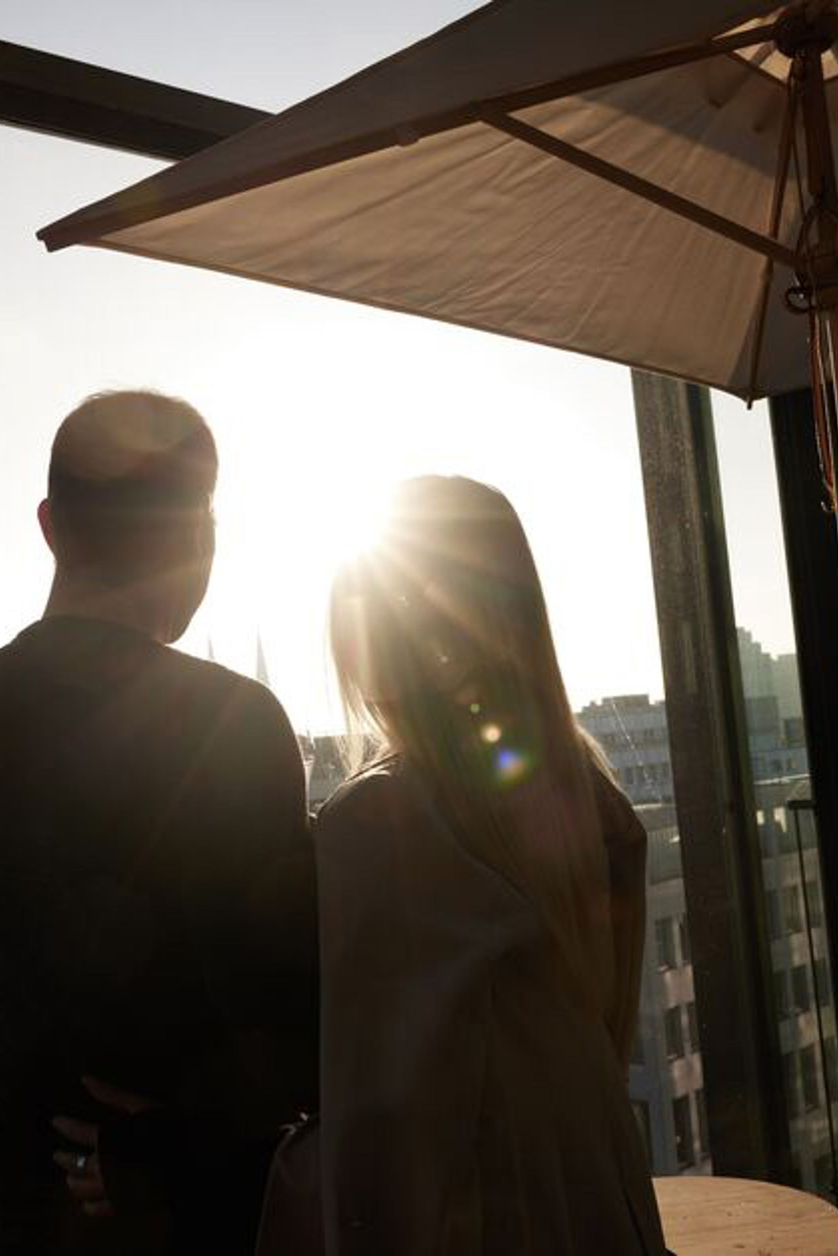 Zwei Personen genießen den Sonnenuntergang gemeinsam auf einer Hotelterrasse mit großem Sonnenschirm und Blick über die Stadt.