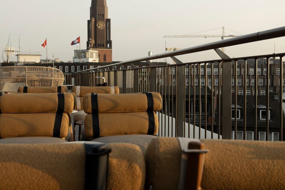 Dachterrasse mit bequemen Sitzgelegenheiten, Blick auf markanten Turm mit Uhr und städtische Gebäude, ruhige Atmosphäre im Abendlicht.