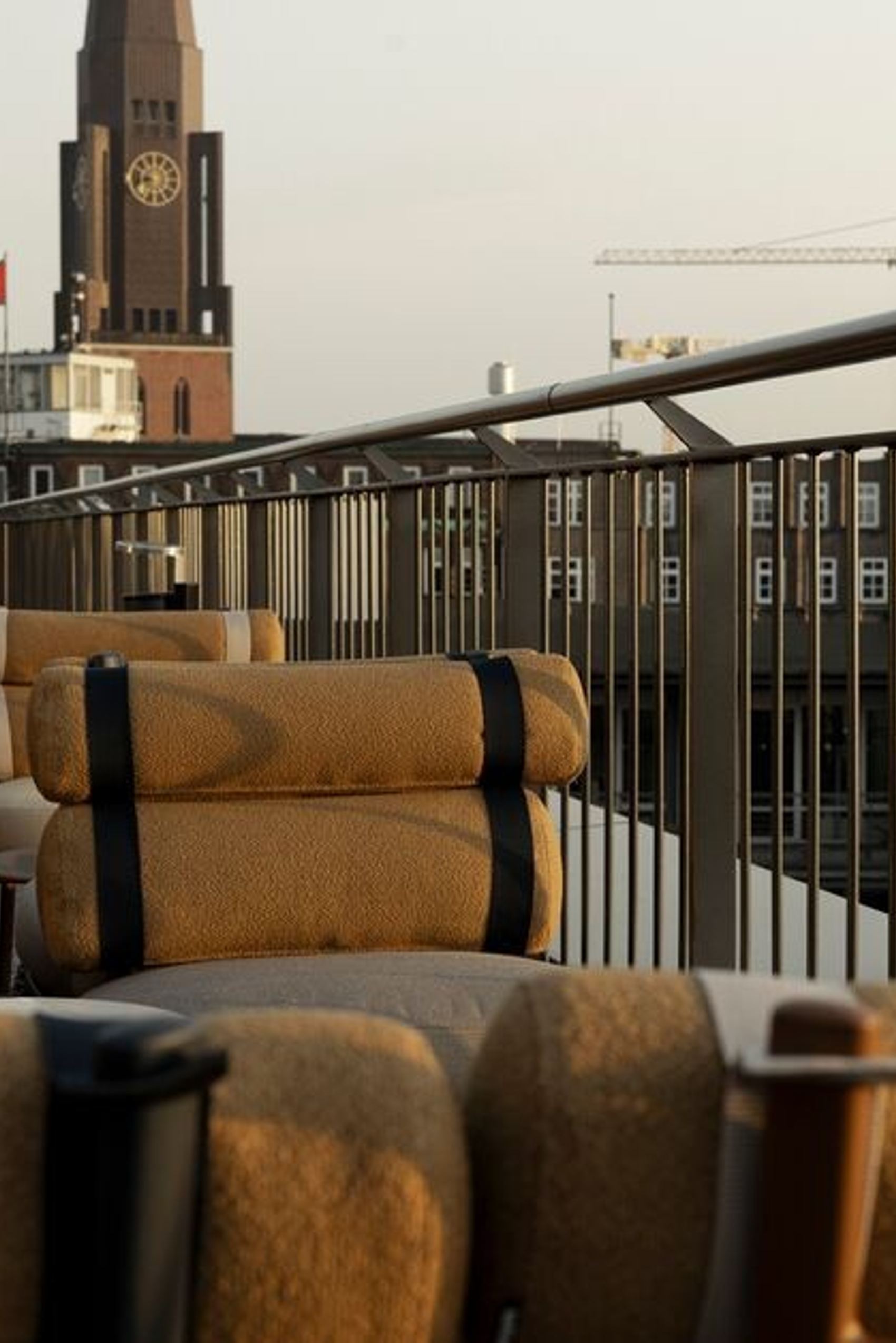 Dachterrasse mit bequemen Sitzgelegenheiten, Blick auf markanten Turm mit Uhr und städtische Gebäude, ruhige Atmosphäre im Abendlicht.