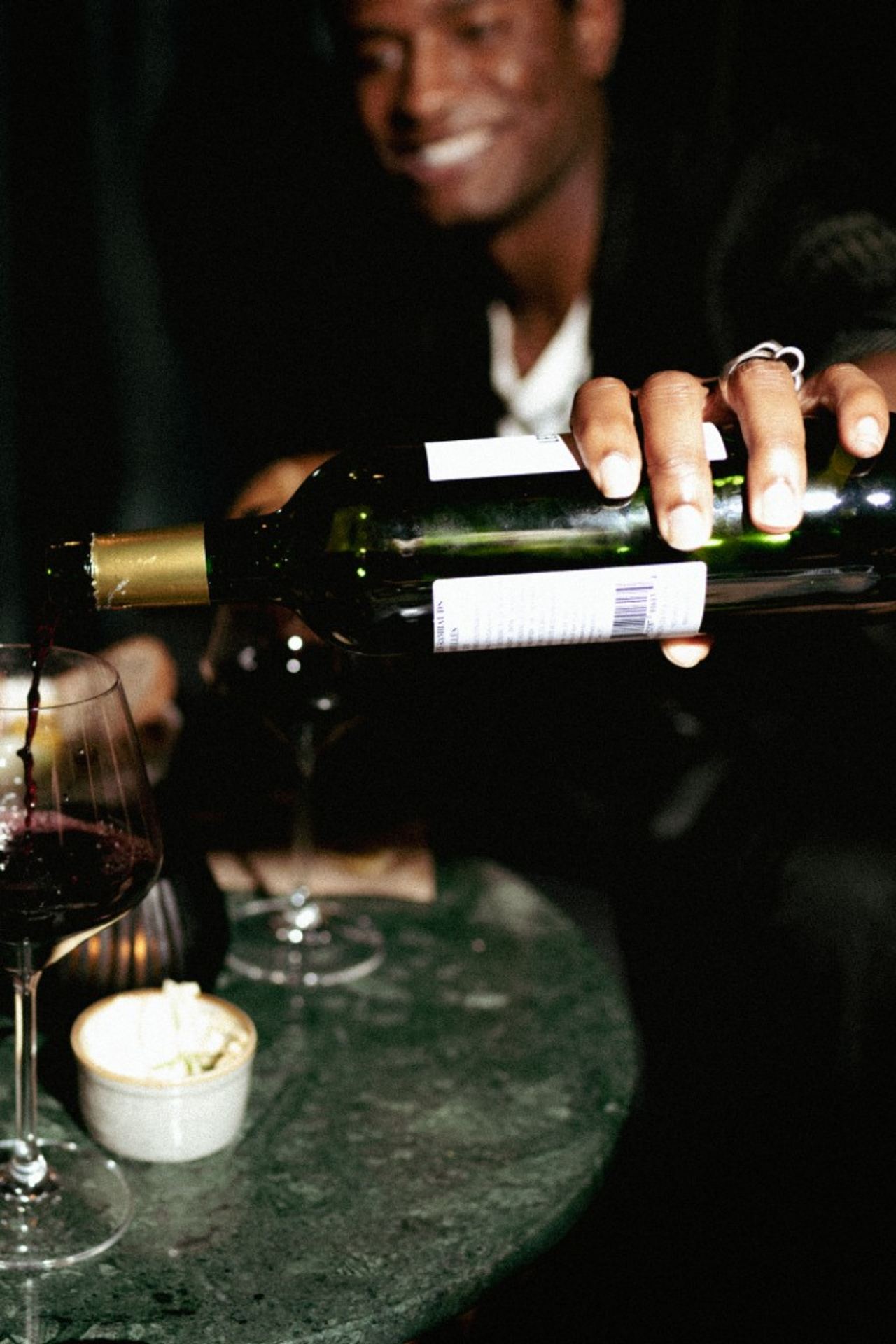 Person gießt Rotwein aus einer Flasche in ein Weinglas auf einem Tisch, der gemütliche Abendstimmung und Genuss vermittelt.