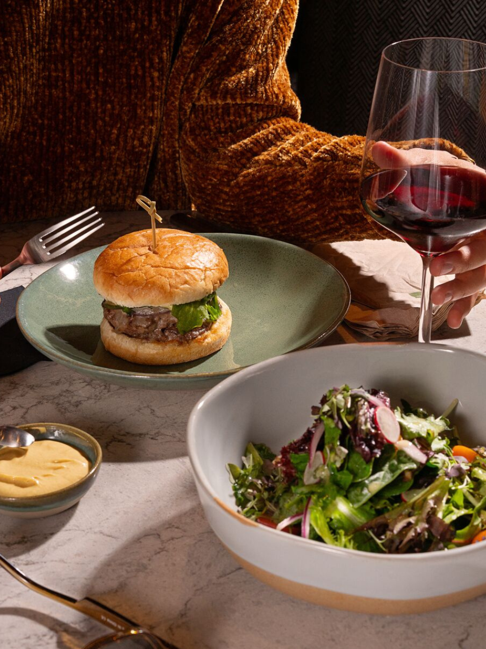 Burger auf einem Teller umrundet von Saucen Wein und Salat