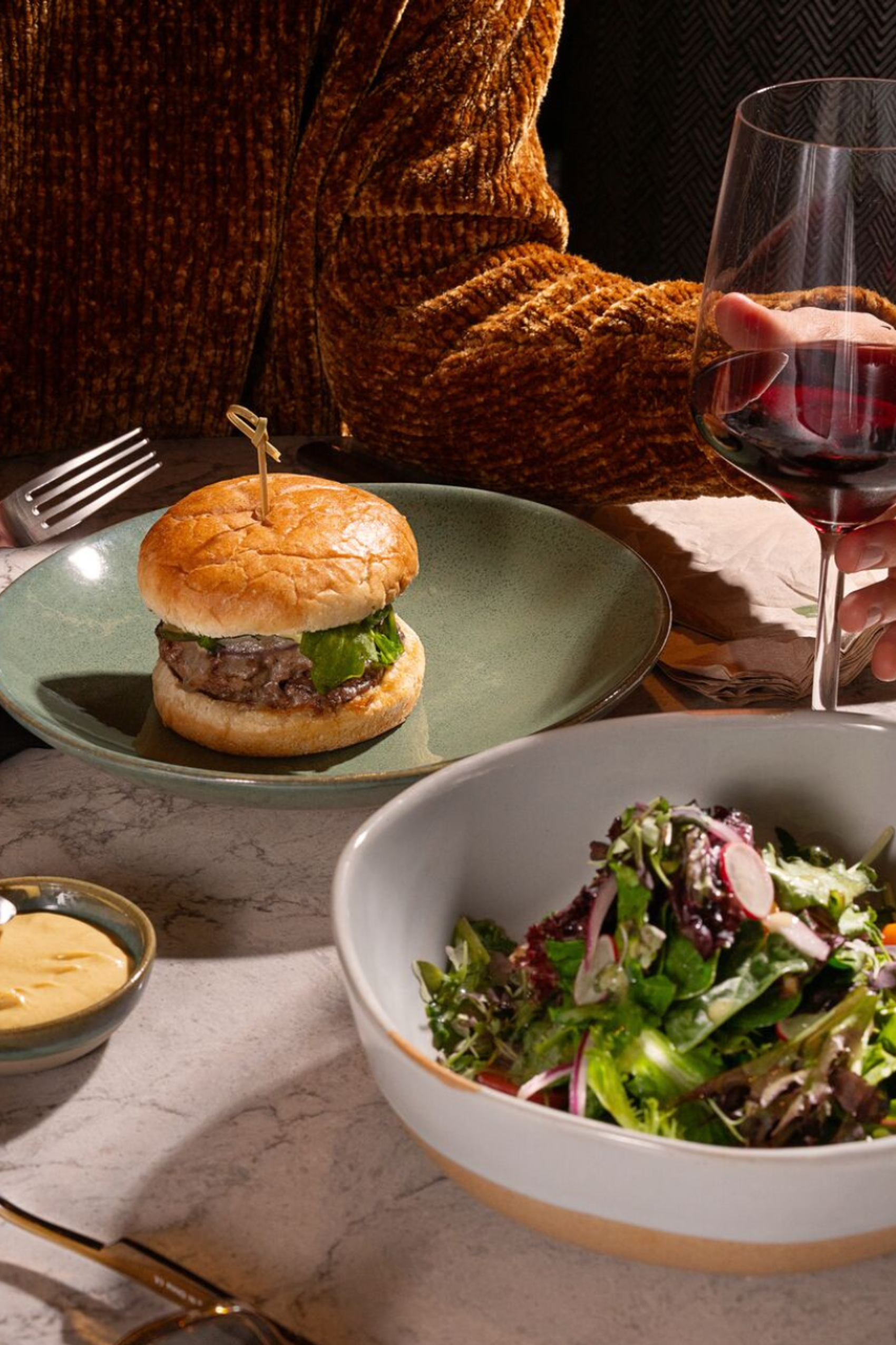 Burger auf einem Teller umrundet von Saucen Wein und Salat