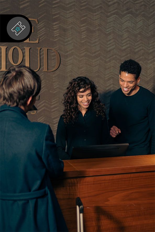 Zwei freundliche Rezeptionisten begrüßen einen Gast an der Hotelrezeption, bereiten den Check-in vor und sorgen für einen angenehmen Empfang.