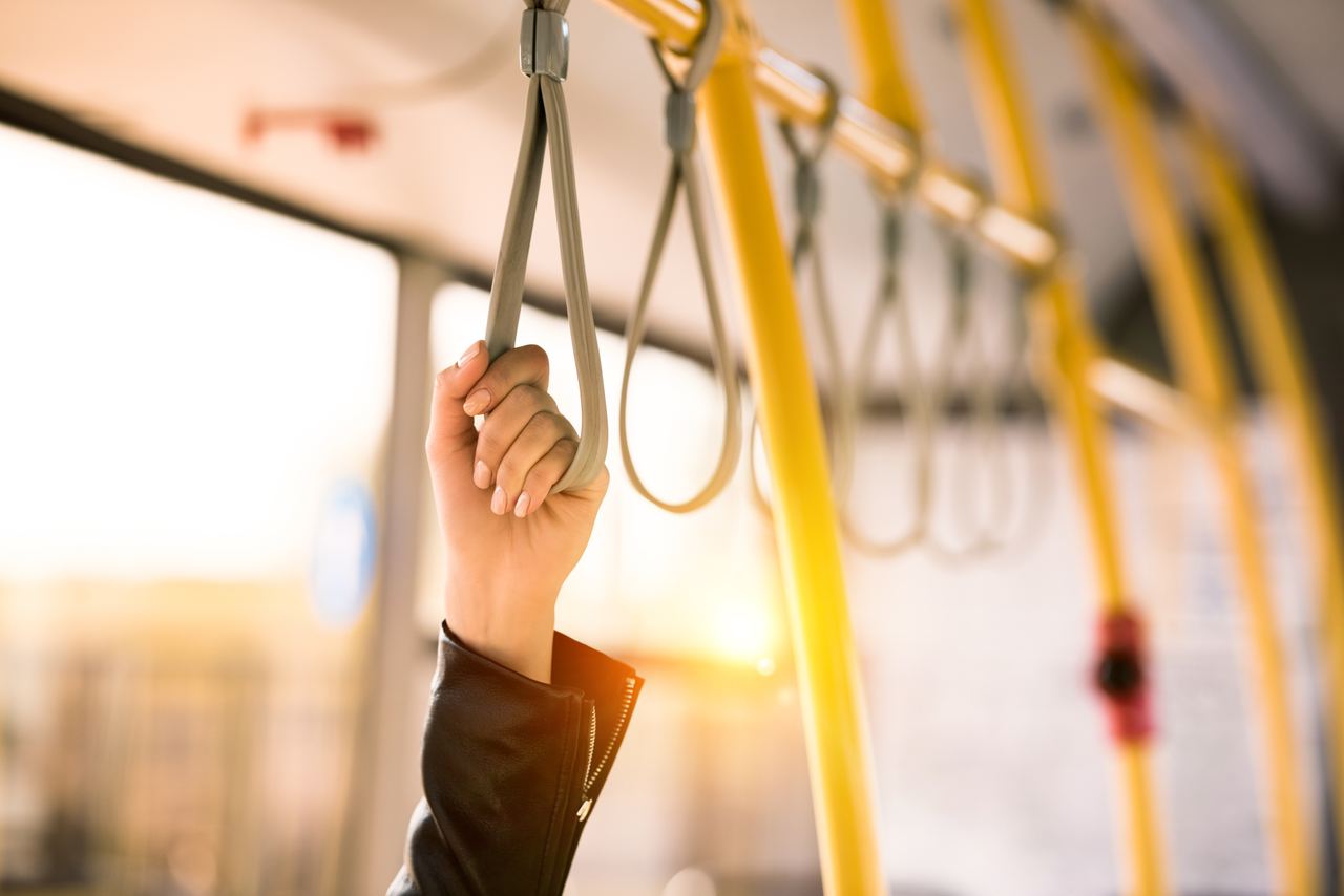 Hand greift in einem Bus an eine Halteschlaufe, warmes Sonnenlicht fällt durch die Fenster, symbolisiert sichere und bequeme Mobilität.