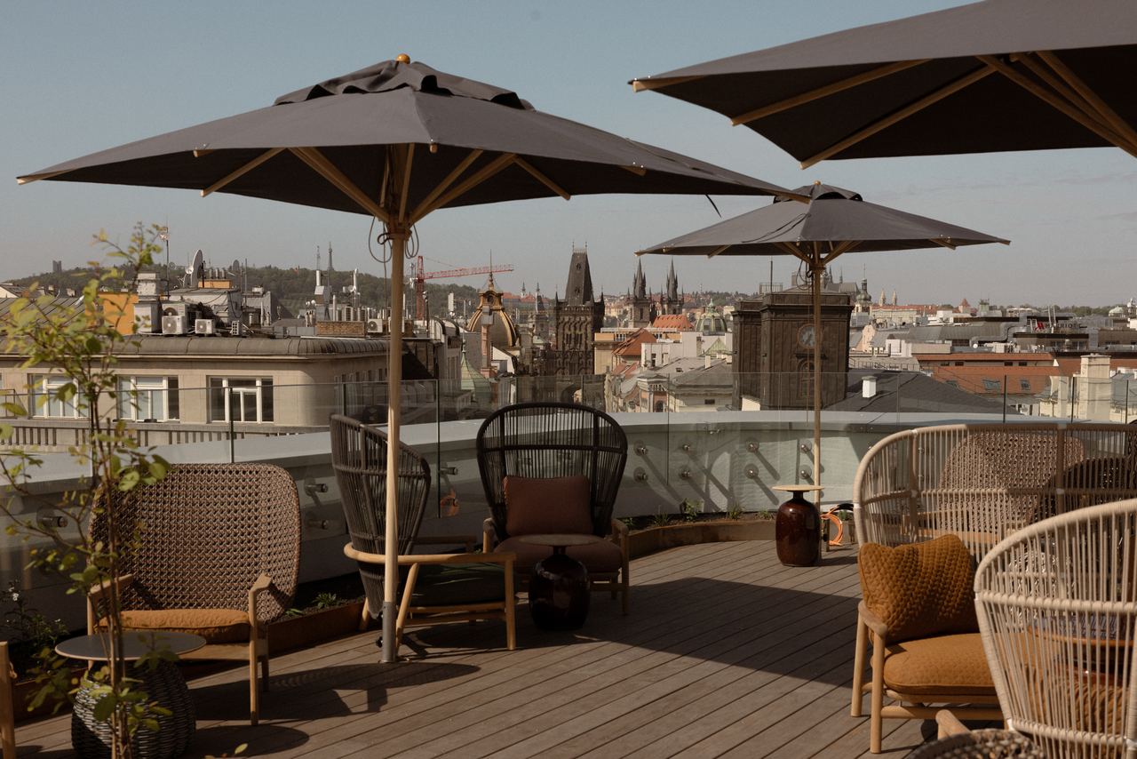 Dachterrasse mit gemütlichen Sitzmöbeln und Sonnenschirmen, bietet entspannte Atmosphäre und weitläufigen Blick über die Stadt mit historischen Gebäuden und Türmen im Hintergrund.