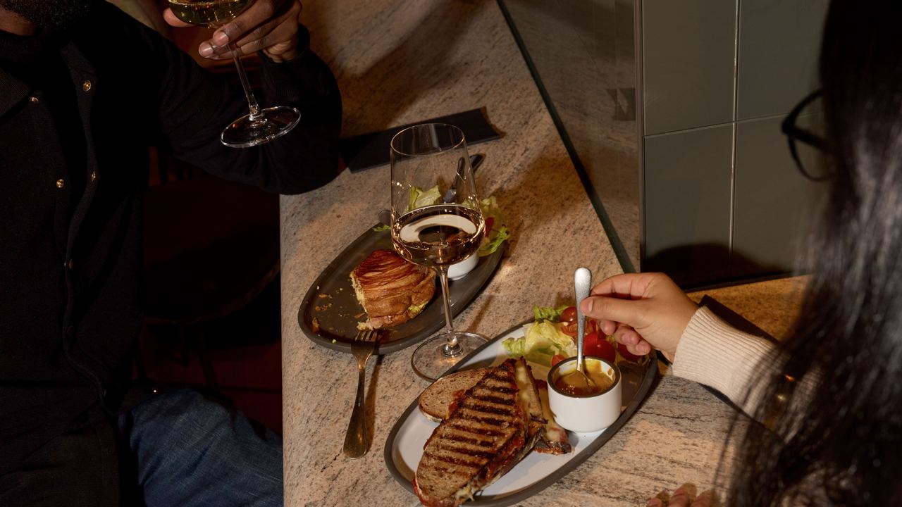 Zwei Personen genießen in gemütlicher Atmosphäre ein Abendessen mit Vorspeisen, warmem Gericht und Wein an einem Marmor-Tresen mit Trennwand.