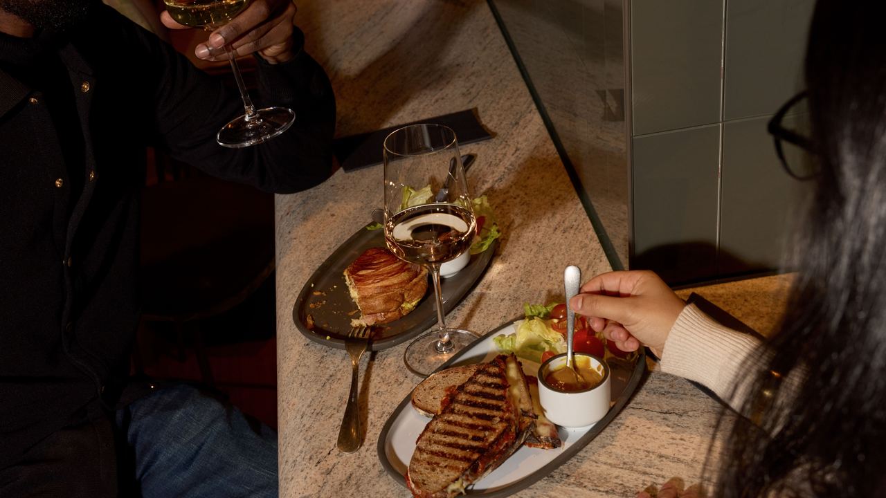 Zwei Personen genießen in gemütlicher Atmosphäre ein Abendessen mit Vorspeisen, warmem Gericht und Wein an einem Marmor-Tresen mit Trennwand. Zwei Personen genießen in gemütlicher Atmosphäre ein Abendessen mit Vorspeisen, warmem Gericht und Wein an einem Marmor-Tresen mit Trennwand.