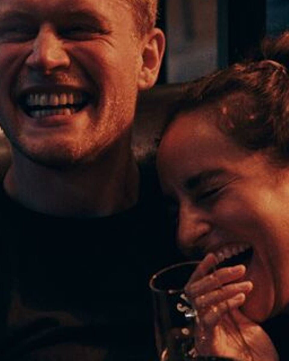 Junges Paar lacht entspannt zusammen, vermittelt Freude und Wohlbefinden während eines gemeinsamen Abends.
