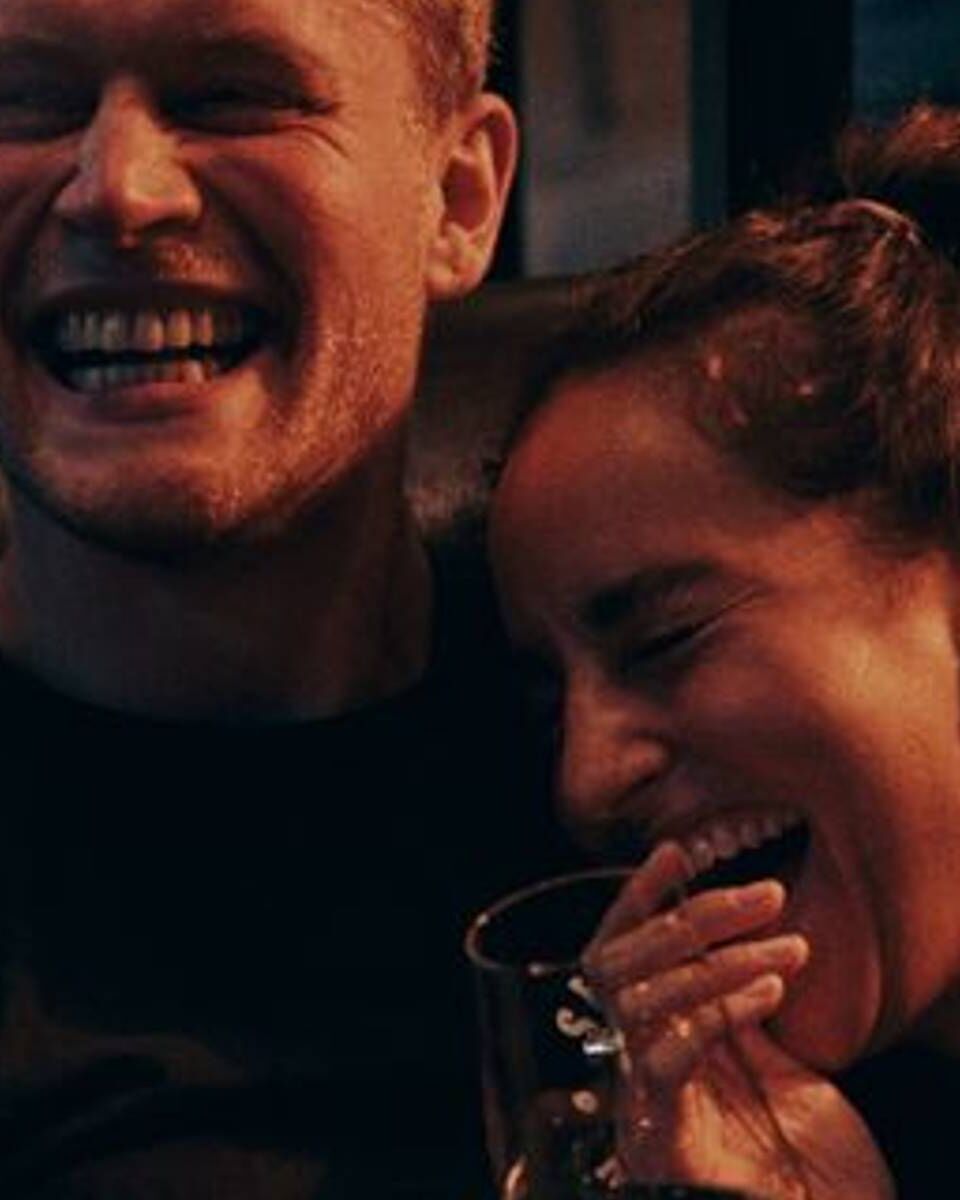 Junges Paar lacht entspannt zusammen, vermittelt Freude und Wohlbefinden während eines gemeinsamen Abends.