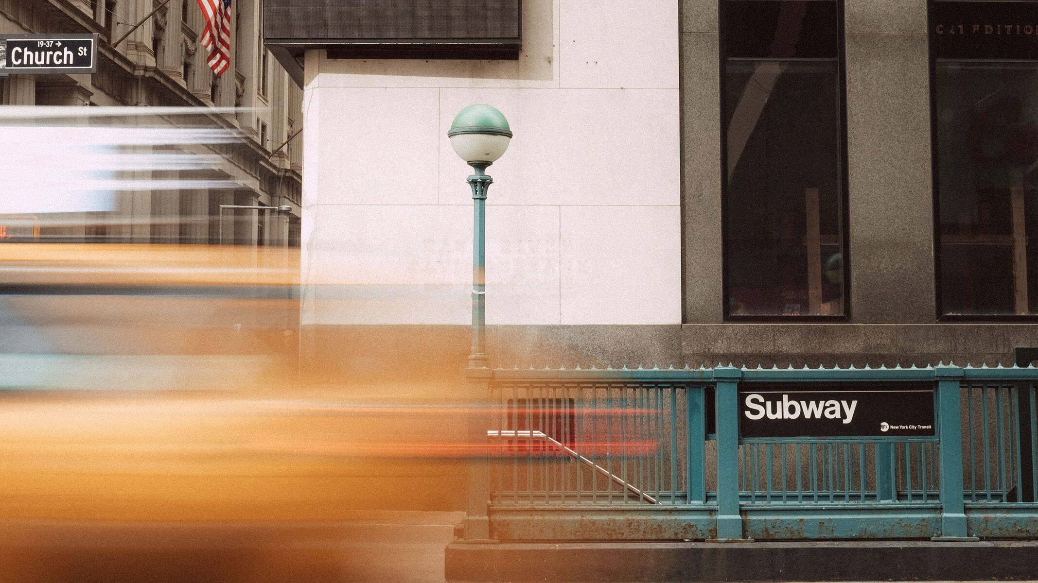 Eingang zur U-Bahn-Station in einer belebten Innenstadt mit vorbeifahrendem Taxi und Fußgängern.