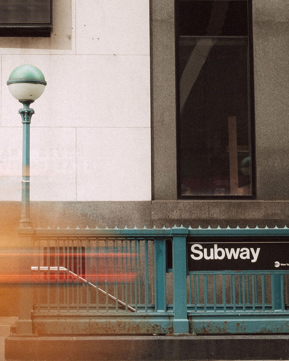 Eingang zur U-Bahn-Station in einer belebten Innenstadt mit vorbeifahrendem Taxi und Fußgängern.