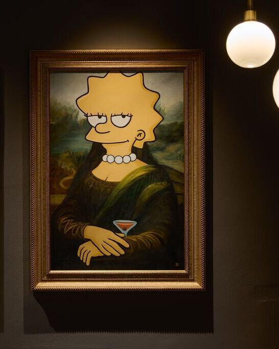Zwei humorvolle Gemälde an der Wand: Links die Mona Lisa mit einem pinken Flamingo in den Armen, rechts Lisa Simpson in der Pose der Mona Lisa, mit einem Cocktailglas in der Hand. Beide Bilder verbinden klassische Kunst mit moderner Popkultur.