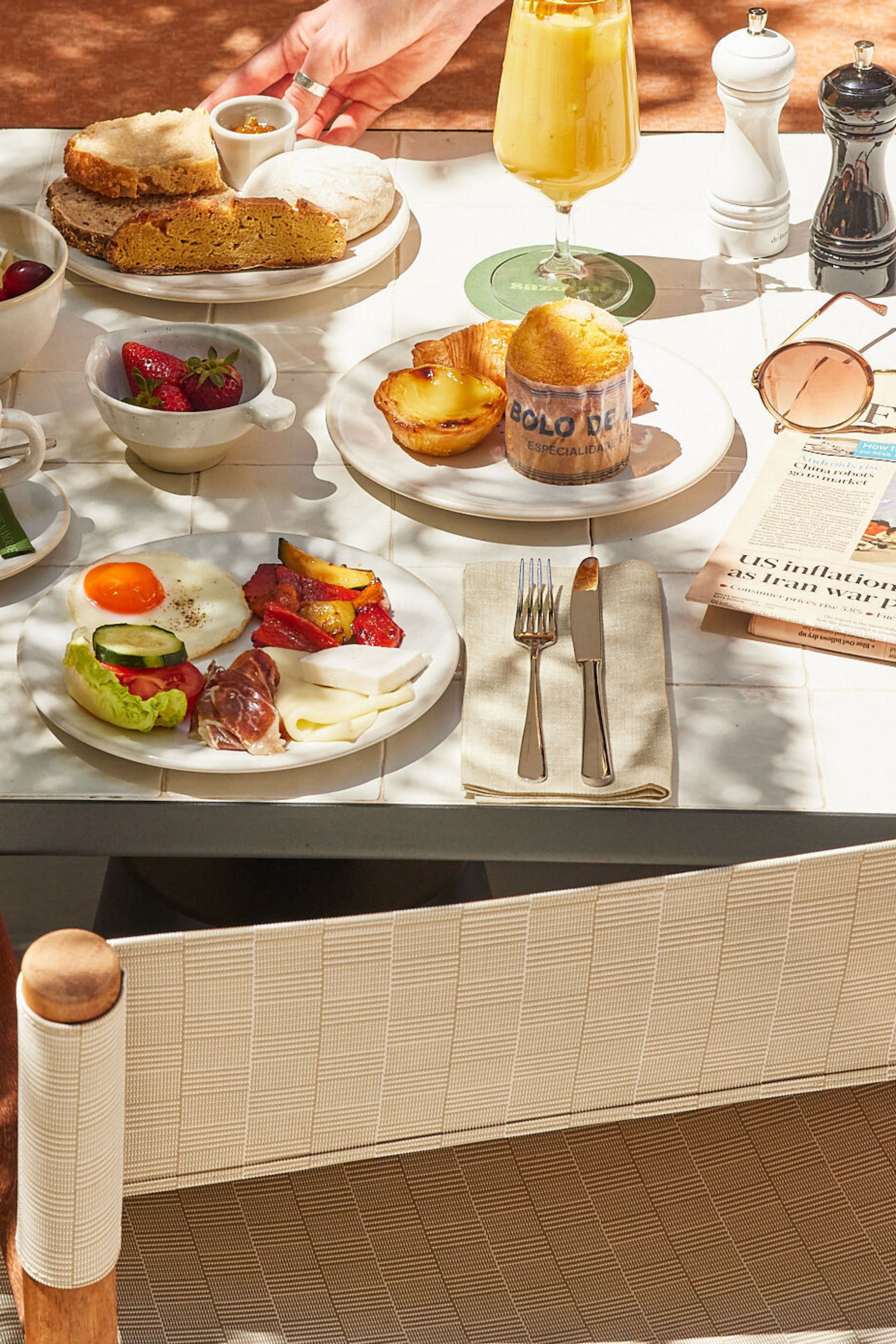 Frühstückstisch mit frischem Gebäck, Kaffee, Müsli, Obst, herzhaften kleinen Speisen und einem Orangensaft in sonniger, gemütlicher Atmosphäre.
