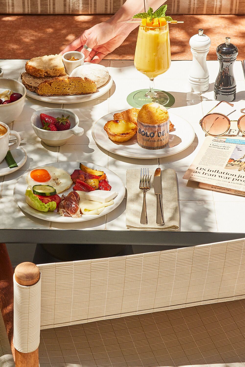 Frühstückstisch mit frischem Gebäck, Kaffee, Müsli, Obst, herzhaften kleinen Speisen und einem Orangensaft in sonniger, gemütlicher Atmosphäre.