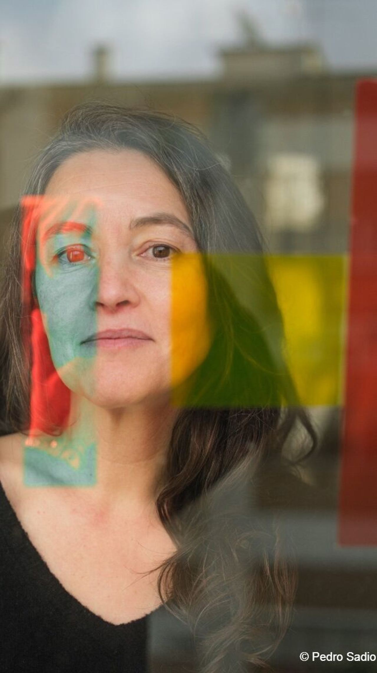 Porträt einer nachdenklichen Frau hinter einer Glasscheibe, durch die sich verschwommene bunte Farbfelder in Rot, Gelb und Grün spiegeln. Porträt einer nachdenklichen Frau hinter einer Glasscheibe, durch die sich verschwommene bunte Farbfelder in Rot, Gelb und Grün spiegeln.