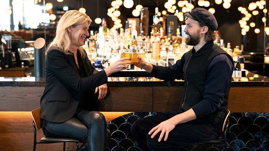 Zwei Gäste stoßen lächelnd mit Getränken an einer eleganten Hotelbar an