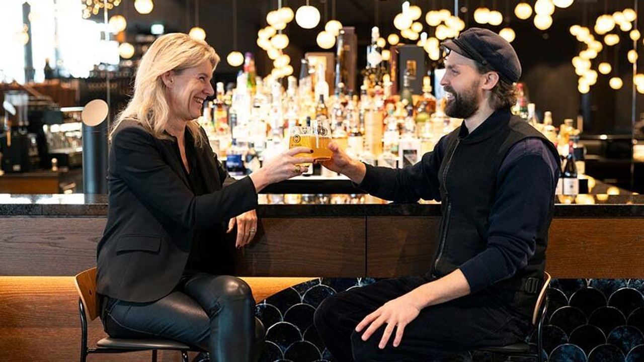 Zwei Gäste stoßen lächelnd mit Getränken an einer eleganten Hotelbar an Zwei Gäste stoßen lächelnd mit Getränken an einer eleganten Hotelbar an