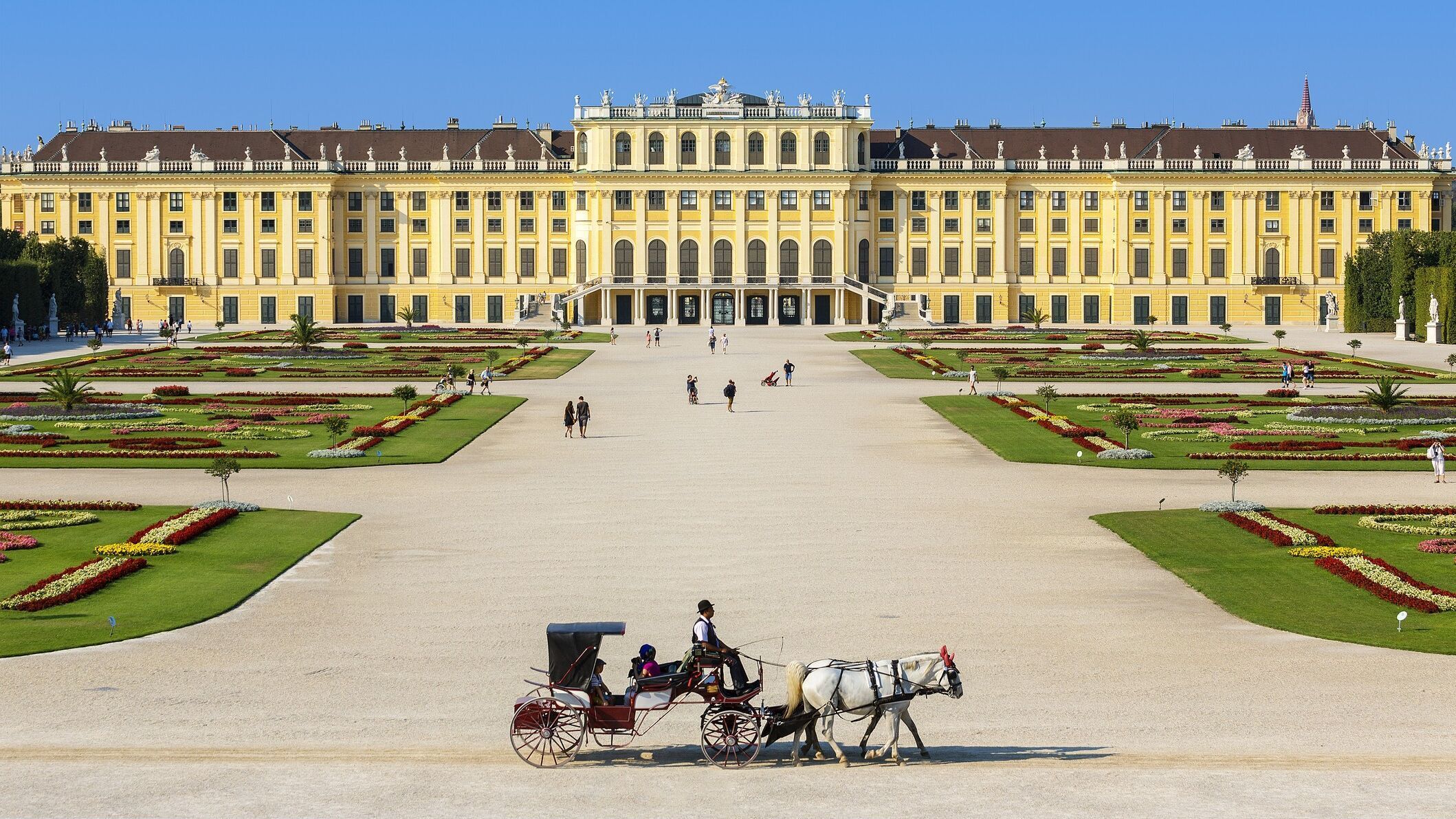 Weitläufiges Barockschloss mit symmetrischem Garten und klaren Wegen, davor eine Pferdekutsche, die eine ruhige, historische Atmosphäre vermittelt.