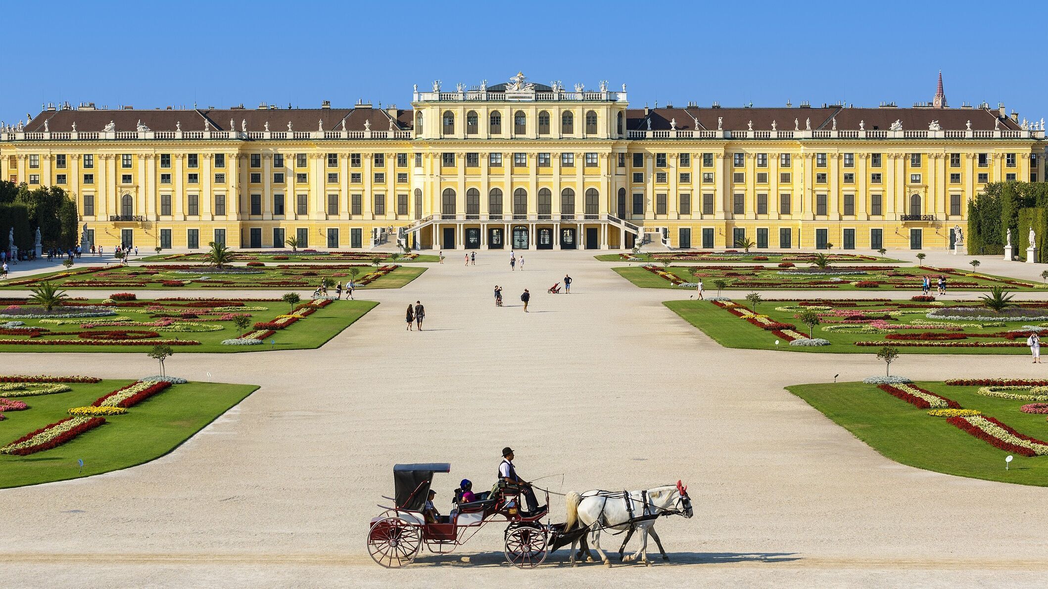 Weitläufiges Barockschloss mit symmetrischem Garten und klaren Wegen, davor eine Pferdekutsche, die eine ruhige, historische Atmosphäre vermittelt.