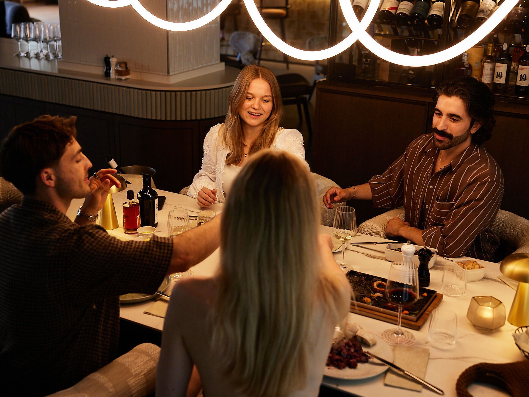 Vier Gäste sitzen an einem elegant gedeckten Tisch, genießen gemeinsames Essen und angeregte Unterhaltung in einem stilvollen Restaurant mit warmem, einladendem Ambiente.