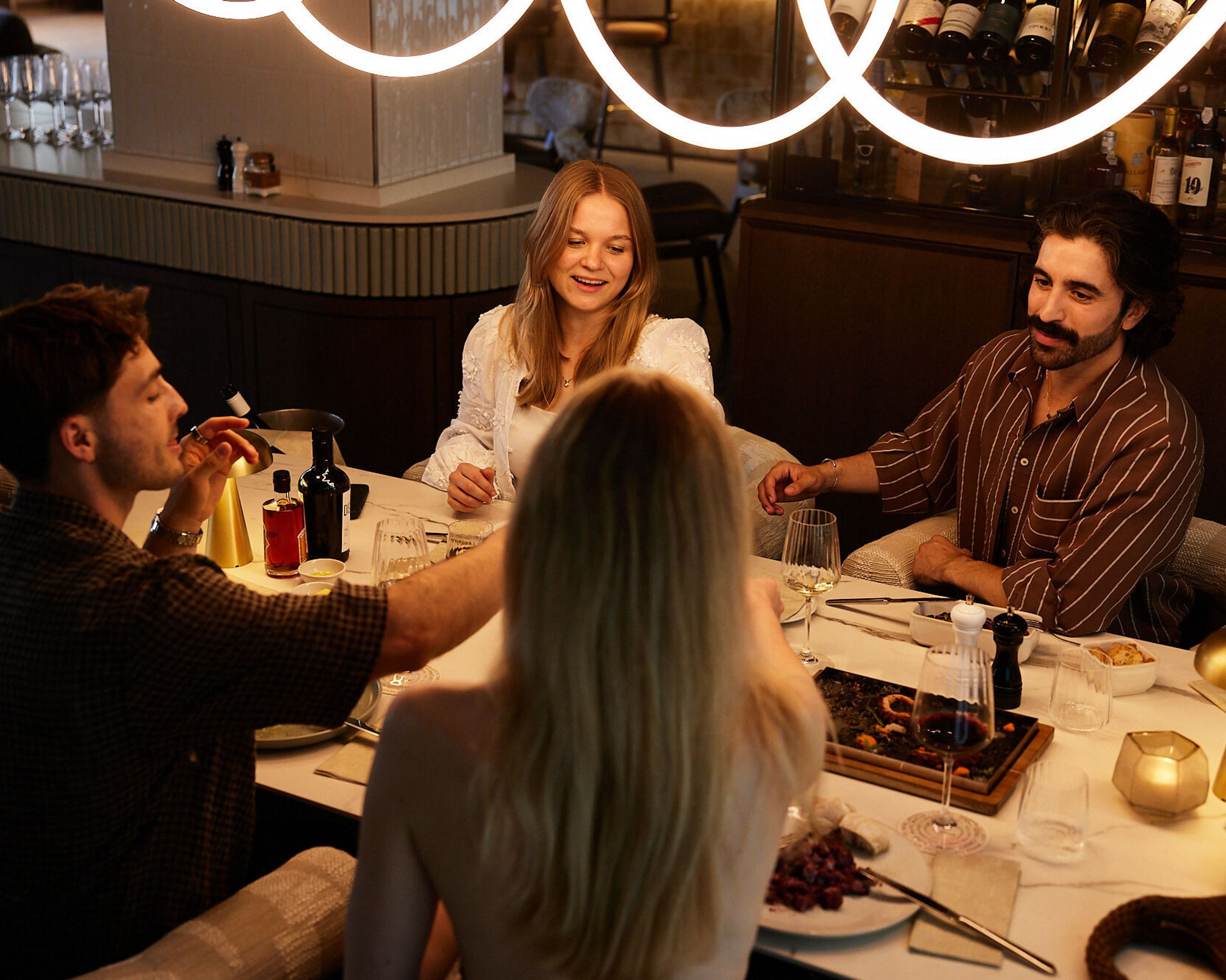 Vier Gäste sitzen an einem elegant gedeckten Tisch, genießen gemeinsames Essen und angeregte Unterhaltung in einem stilvollen Restaurant mit warmem, einladendem Ambiente.