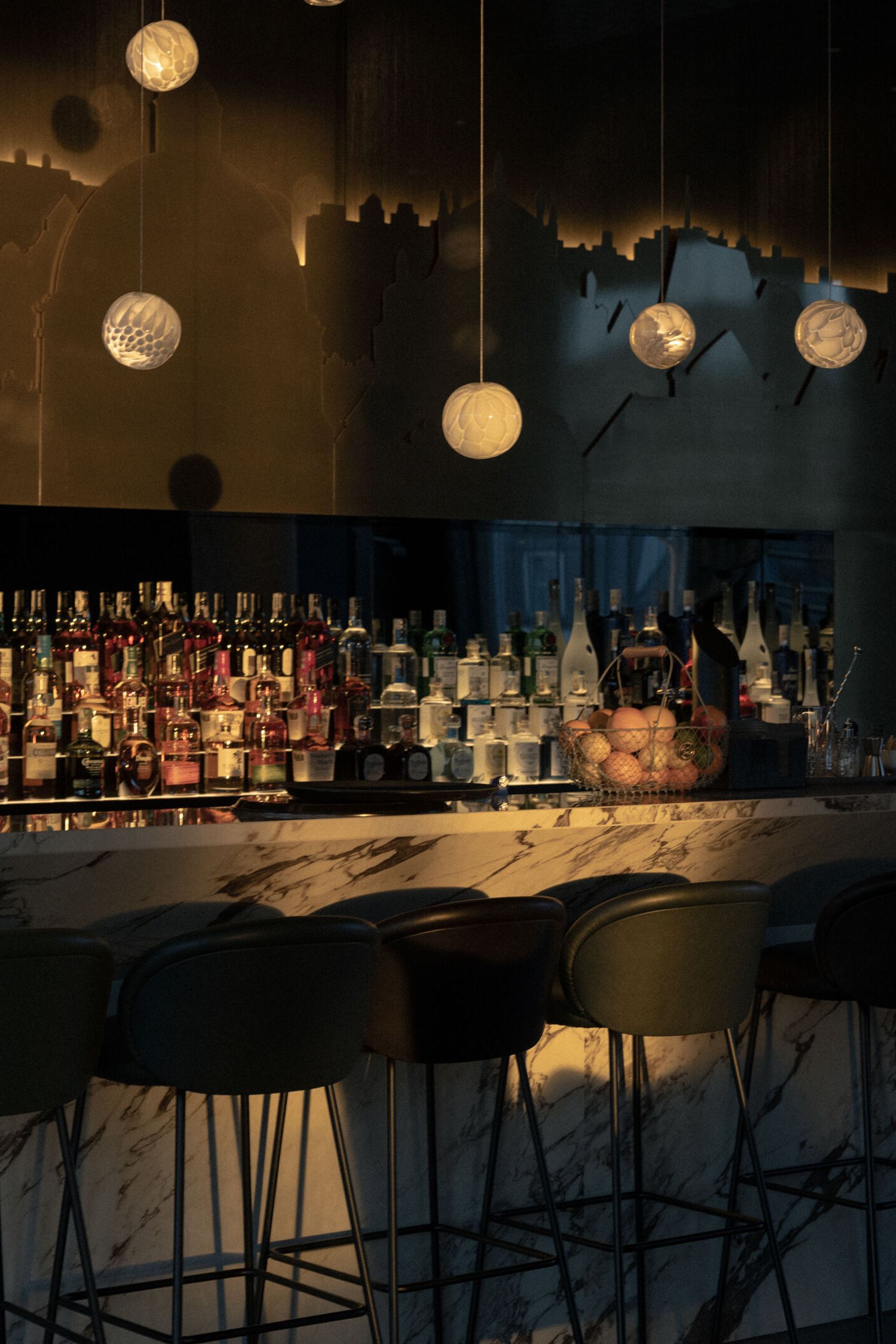Hotelbar mit gedämpfter Beleuchtung, modernen Hockern und einem langen Marmor-Bar-Tresen, darüber hängen dekorative, kugelförmige Pendelleuchten