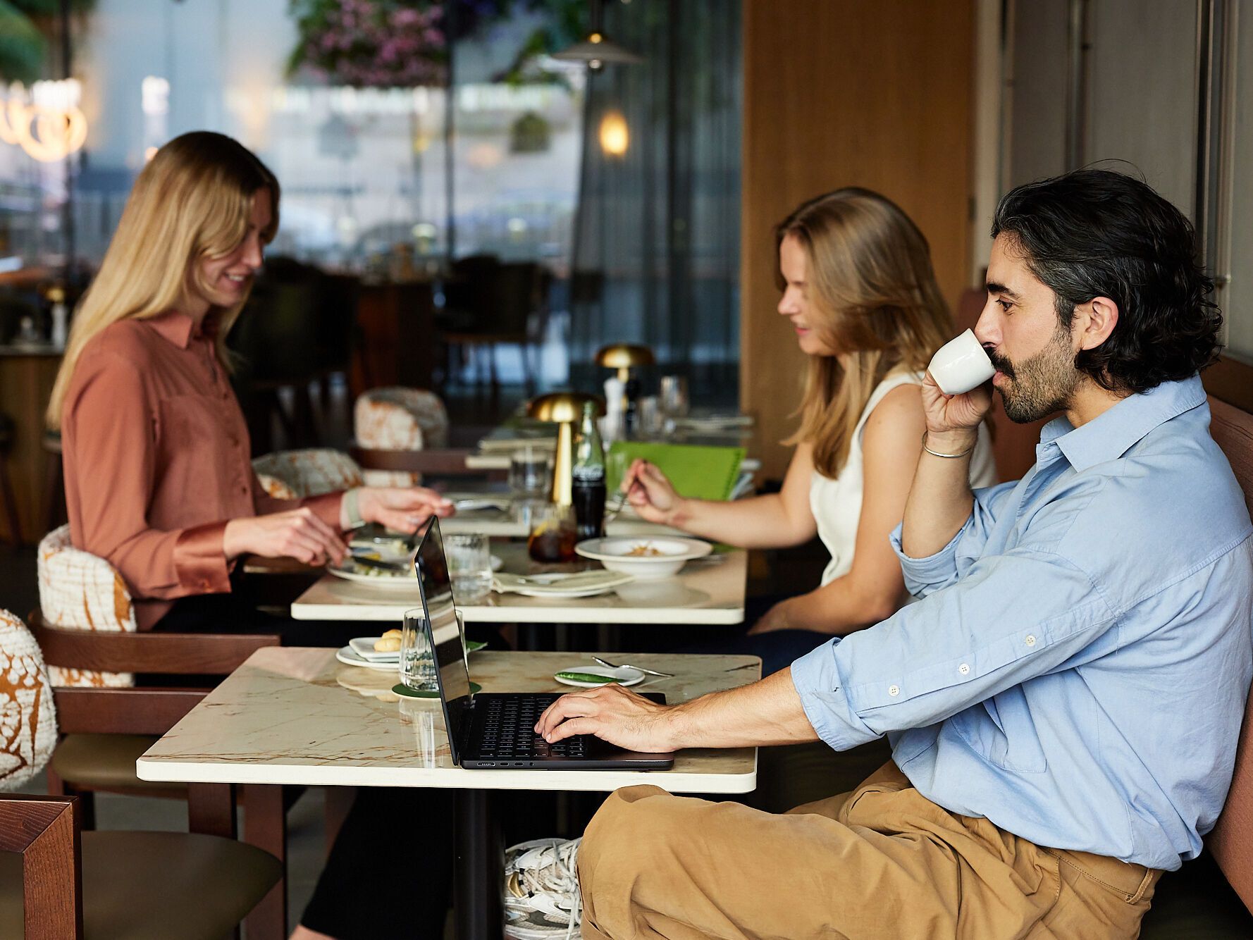 Drei entspannte Gäste genießen im stilvollen Café Frühstück und Kaffee, zwei arbeiten am Laptop, die Atmosphäre wirkt ruhig und einladend.