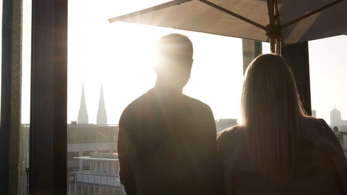 Hotel Düsseldorf KöBogen The Cloud One zwei Personen schauen aus einem hohen Fenster mit Sonne
