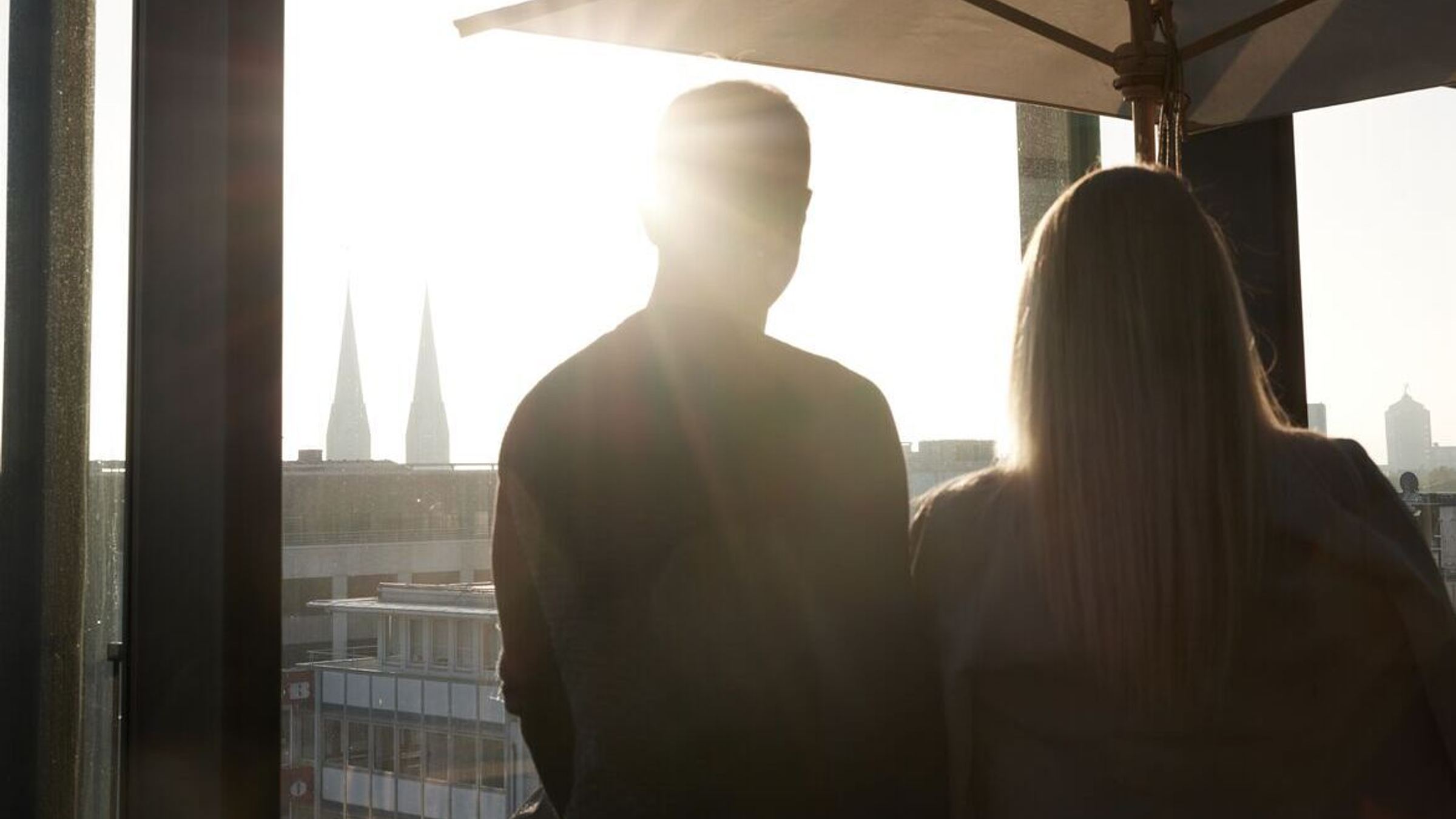 Hotel Düsseldorf KöBogen The Cloud One zwei Personen schauen aus einem hohen Fenster mit Sonne Hotel Düsseldorf KöBogen The Cloud One zwei Personen schauen aus einem hohen Fenster mit Sonne
