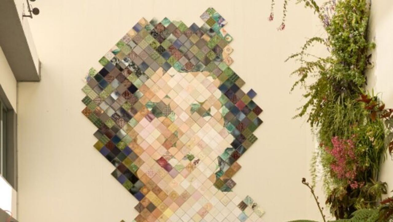 Großes Wandkunstwerk aus bunten Quadraten, das ein Frauenportrait darstellt, im hellen, modernen Innenhof mit Sitzgelegenheiten und üppigen grünen Pflanzen. Großes Wandkunstwerk aus bunten Quadraten, das ein Frauenportrait darstellt, im hellen, modernen Innenhof mit Sitzgelegenheiten und üppigen grünen Pflanzen.