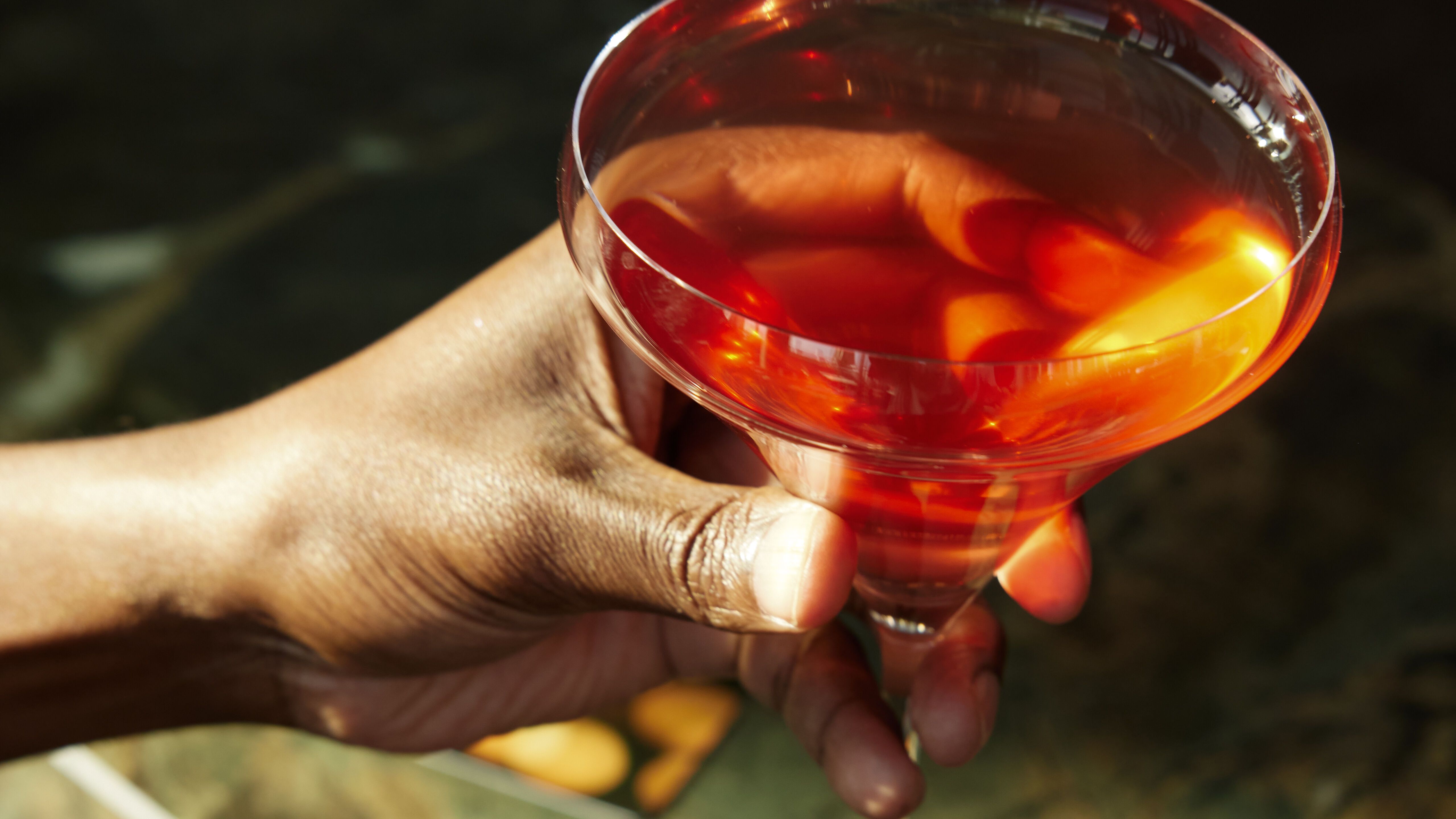 Hand hält ein elegant servierten Cocktail in einem stilvollen Martiniglas, auf einem marmornen Tresen, vermittelt Atmosphäre von Entspannung und Genuss in barähnlicher Umgebung.