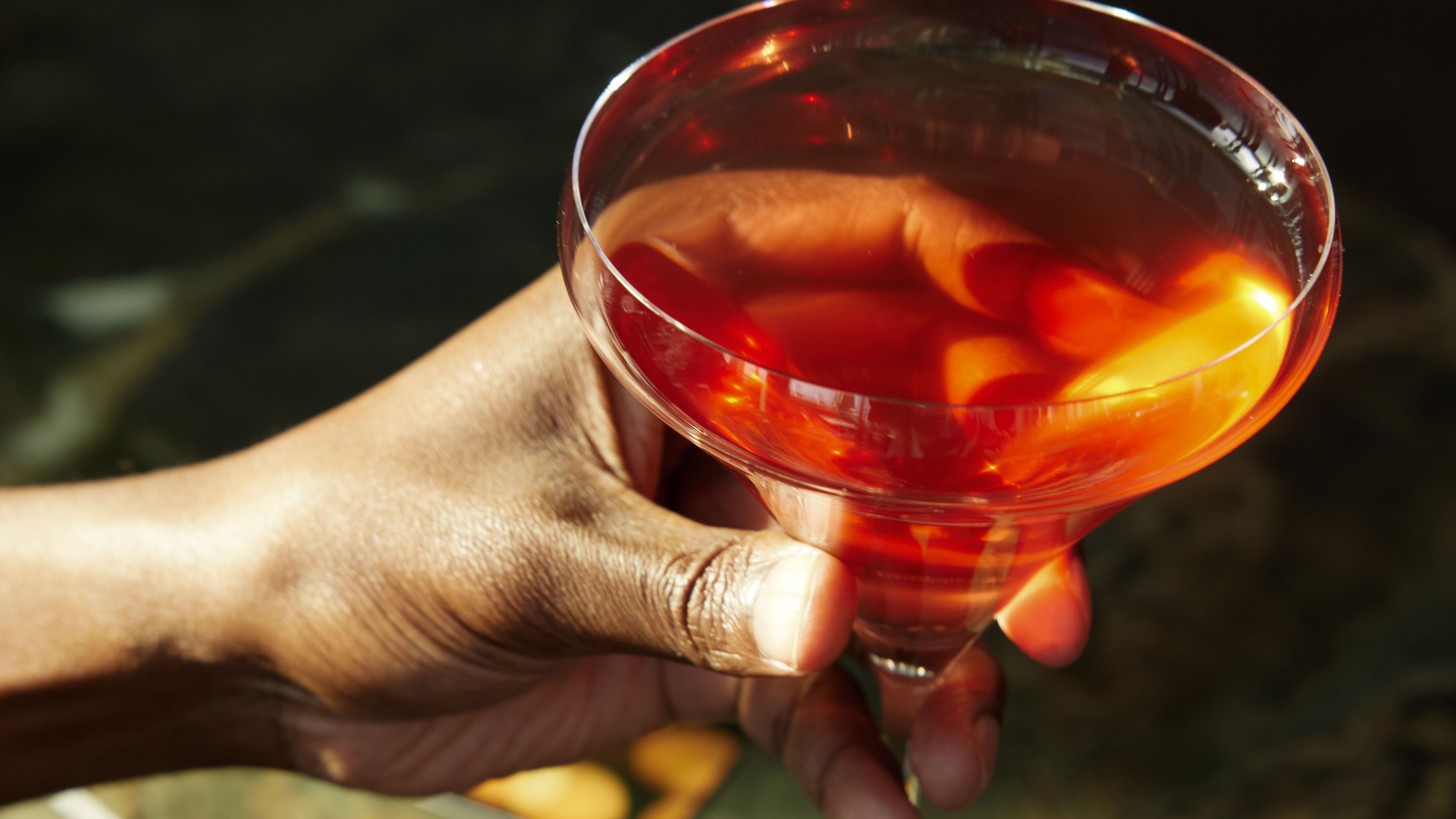 Hand hält ein elegant servierten Cocktail in einem stilvollen Martiniglas, auf einem marmornen Tresen, vermittelt Atmosphäre von Entspannung und Genuss in barähnlicher Umgebung.
