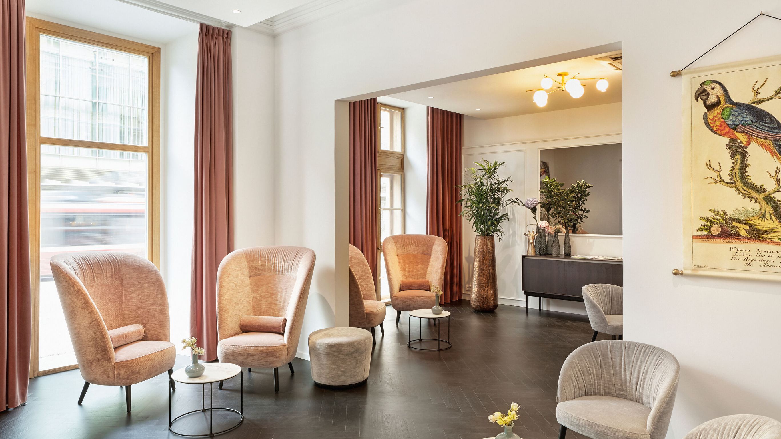 Helle, stilvoll eingerichtete Lounge mit bequemen Sesseln, kleinen Tischen und großen Fenstern, die viel Tageslicht bieten. Dezente Dekoration und Pflanzen schaffen eine einladende Atmosphäre zum Entspannen und Verweilen.