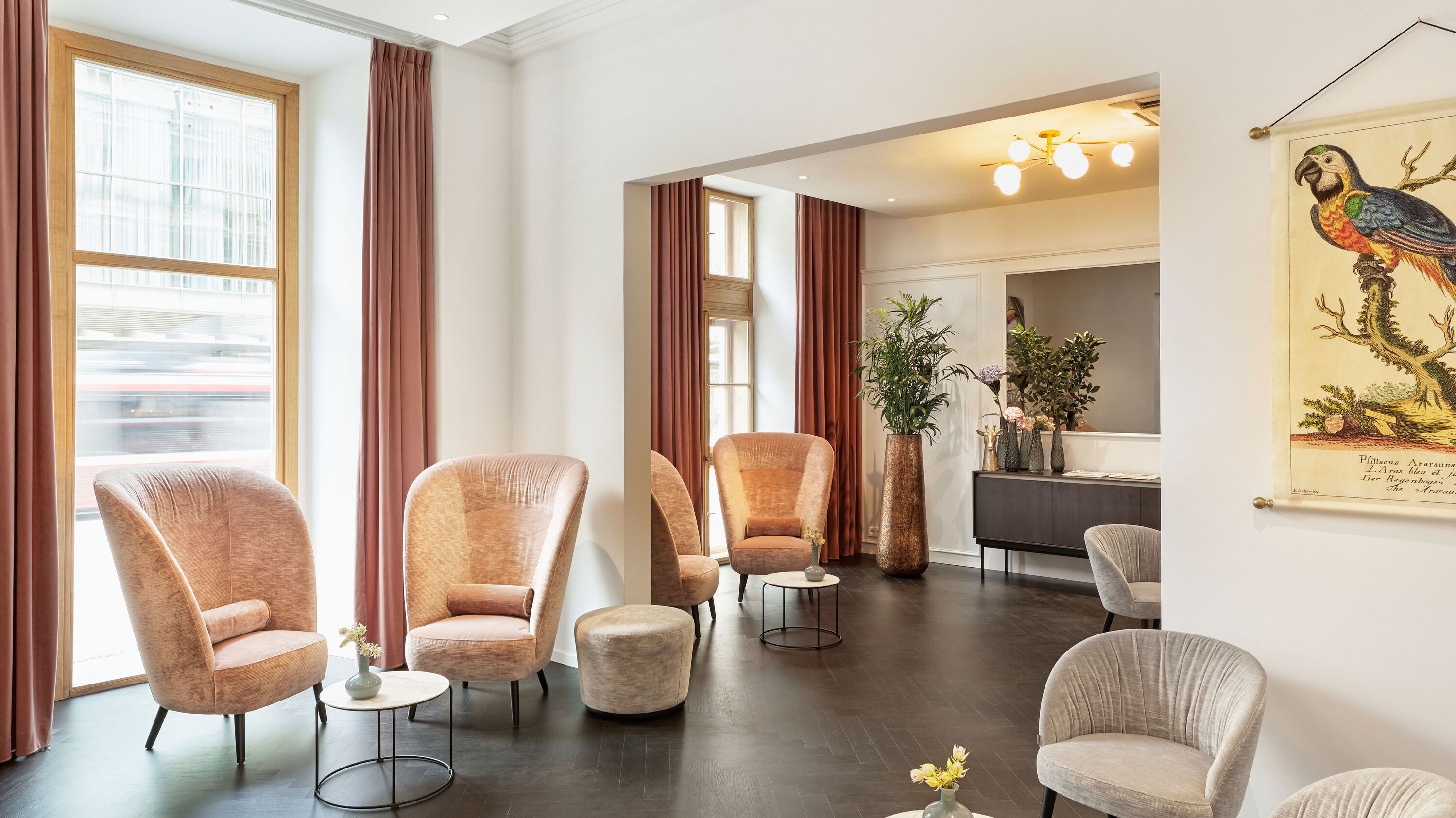 Helle, stilvoll eingerichtete Lounge mit bequemen Sesseln, kleinen Tischen und großen Fenstern, die viel Tageslicht bieten. Dezente Dekoration und Pflanzen schaffen eine einladende Atmosphäre zum Entspannen und Verweilen.