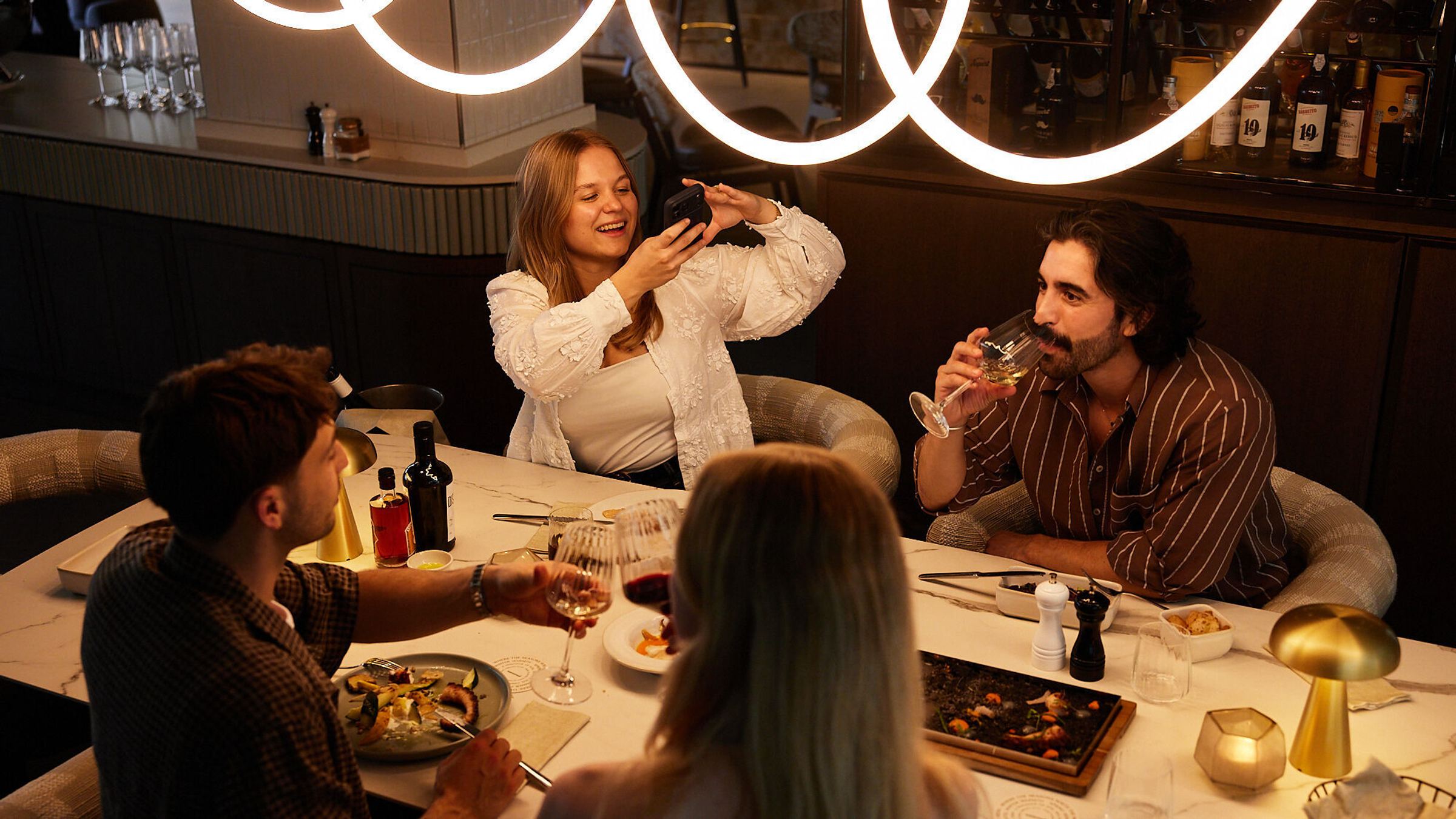 Vier Personen genießen entspannt ein Abendessen in stilvollem Restaurantambiente, lachen und teilen Momente bei Wein und leckeren Speisen.