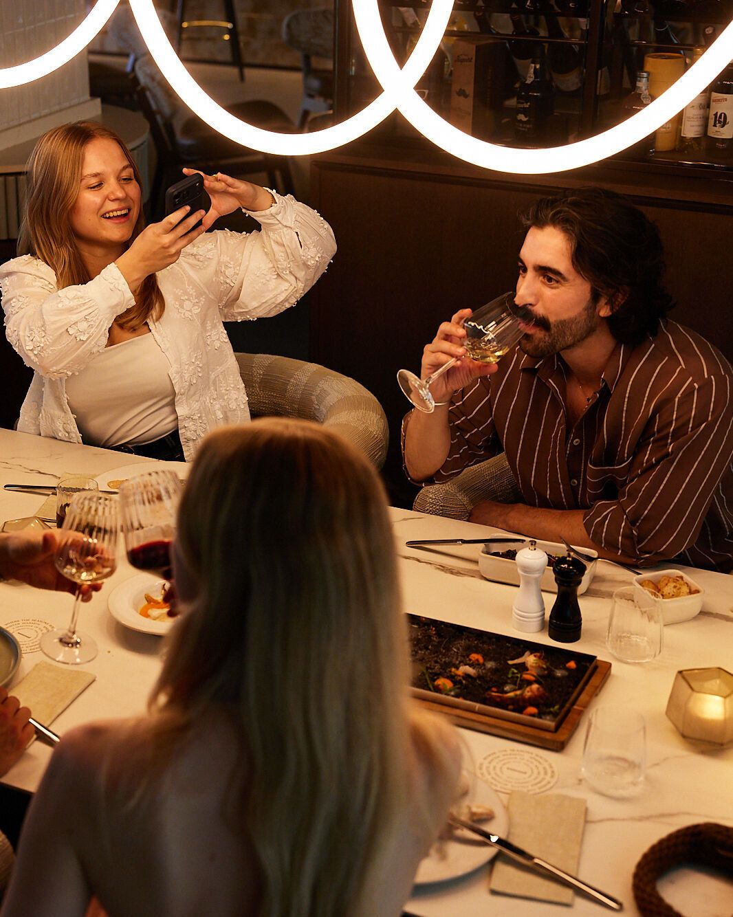 Vier Personen genießen entspannt ein Abendessen in stilvollem Restaurantambiente, lachen und teilen Momente bei Wein und leckeren Speisen.