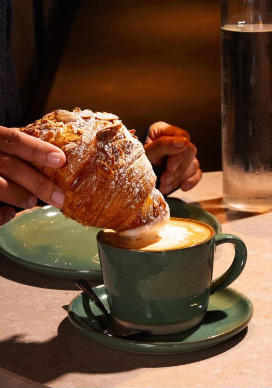 Frau tunkt Croissant in Kaffee beim Frühstück