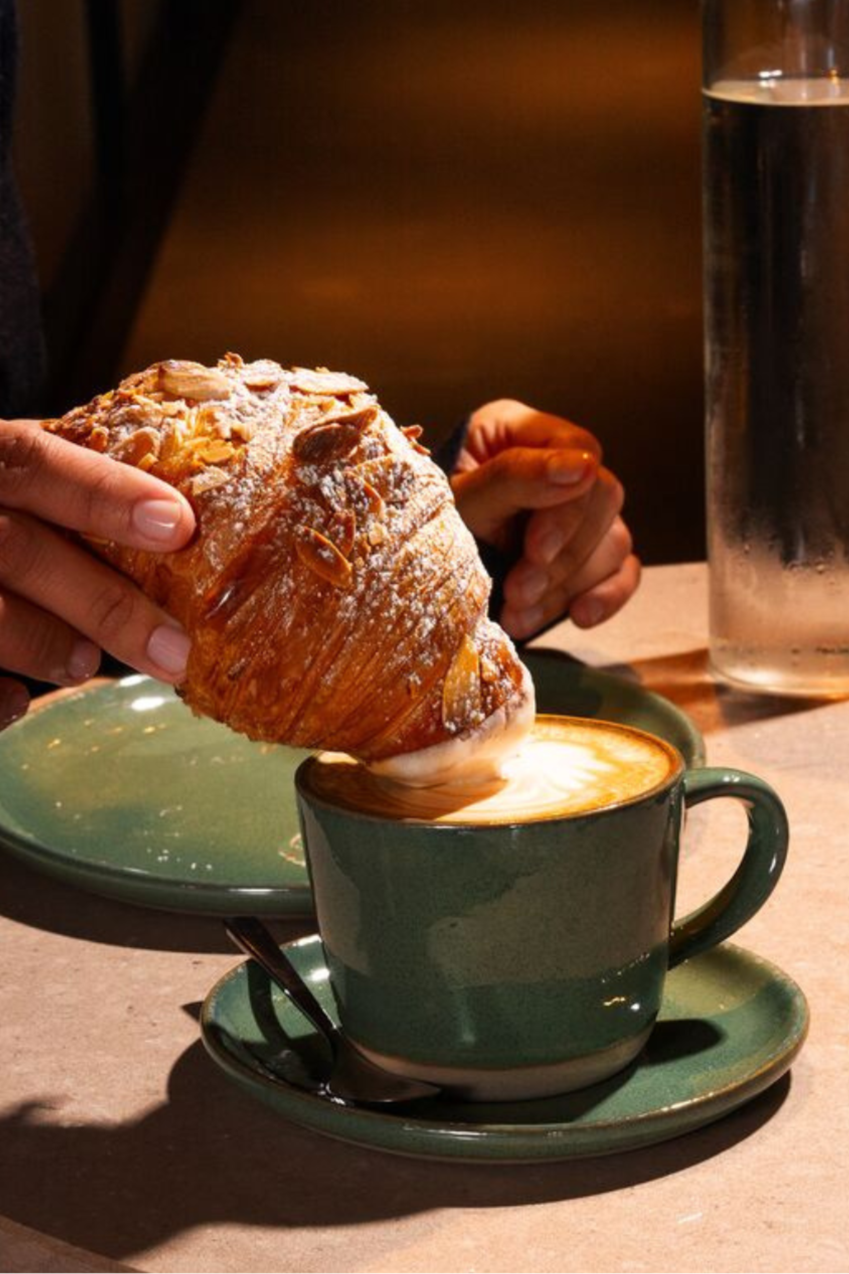 Frau tunkt Croissant in Kaffee beim Frühstück