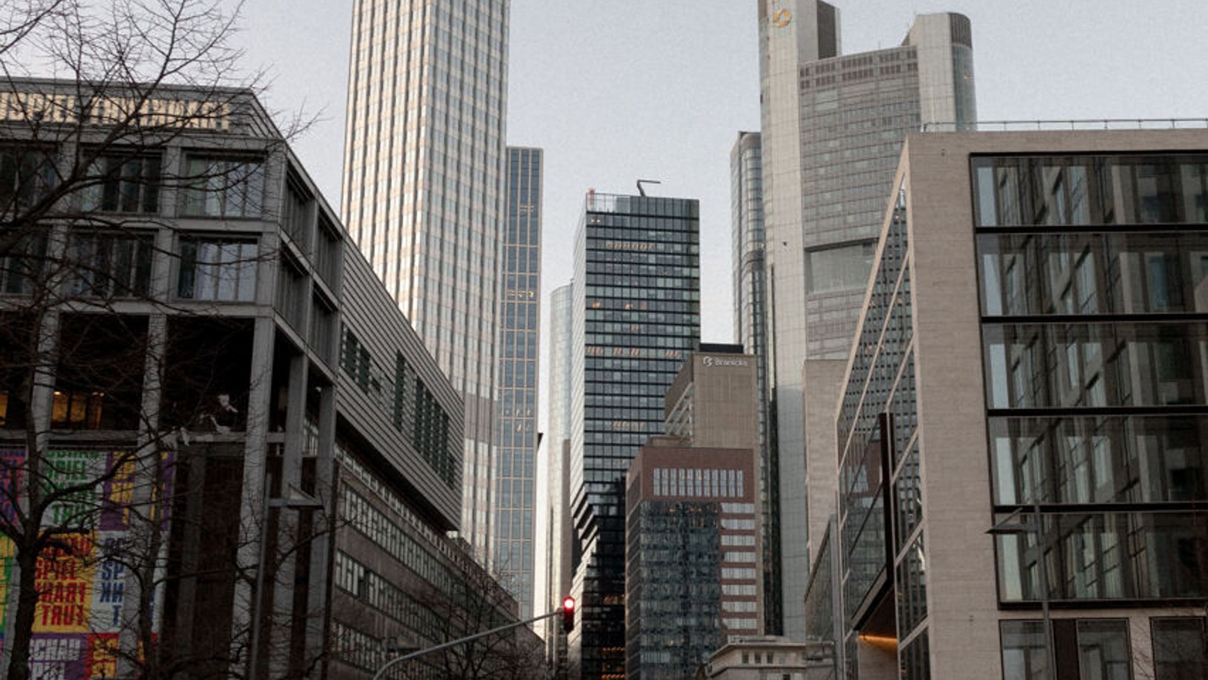 Straße in einem urbanen Geschäftsviertel mit modernen Hochhäusern und Bürogebäuden, vereinzelten Fußgängern und schwachem Tageslicht an einem bewölkten Tag. Straße in einem urbanen Geschäftsviertel mit modernen Hochhäusern und Bürogebäuden, vereinzelten Fußgängern und schwachem Tageslicht an einem bewölkten Tag.