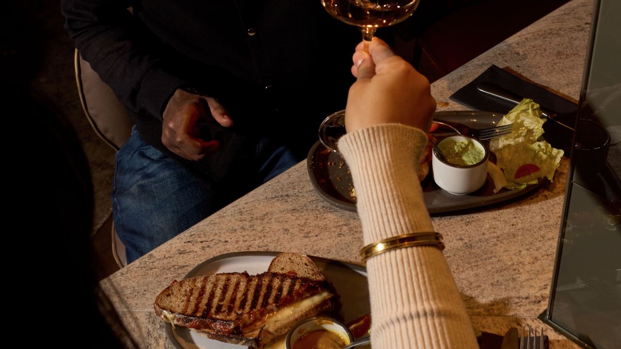 Zwei Personen stoßen in einem gemütlichen Restaurant bei gedämpftem Licht mit Weingläsern an. Auf dem Tisch liegen Teller mit Essen und Dips, Atmosphäre ist entspannt und einladend, ideal für einen genussvollen Abend zu zweit.